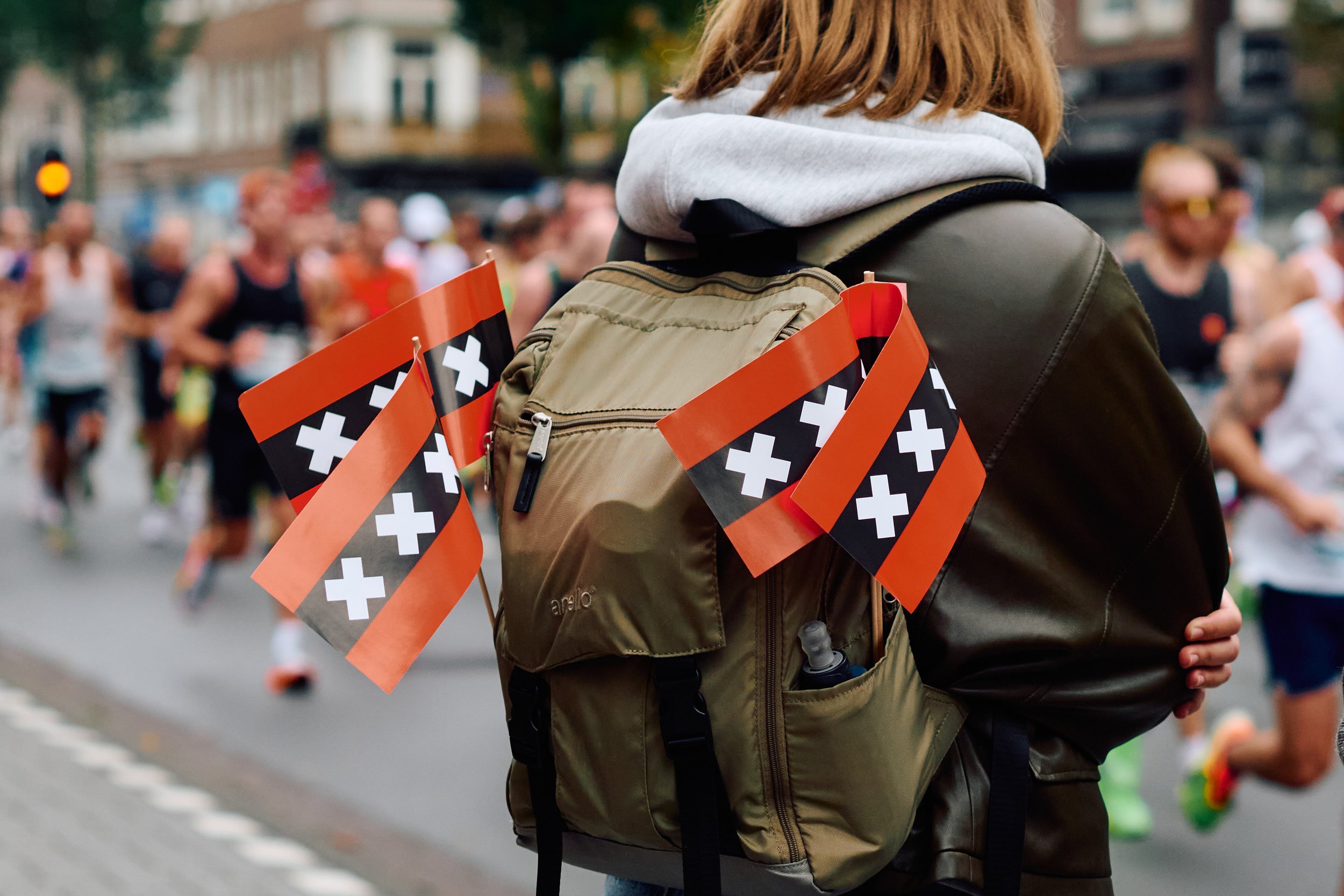 Person with a backpack standing among marathon runners, with Swiss flags attached to the backpack.