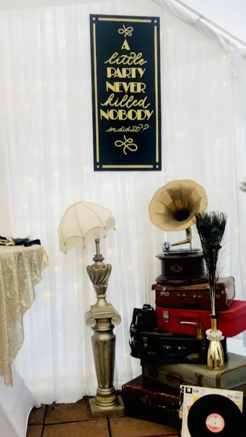 1920s inspired hand-painted sign in gold on black, featuring the quote "A little party never killed nobody, or did it?"