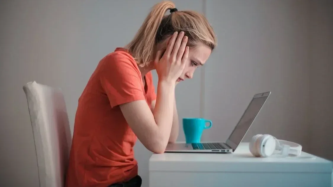 Frau sitzt erschöpft vor dem Laptop und hält die Hände am Kopf als Symbol für emotionalen Stress durch toxische Menschen