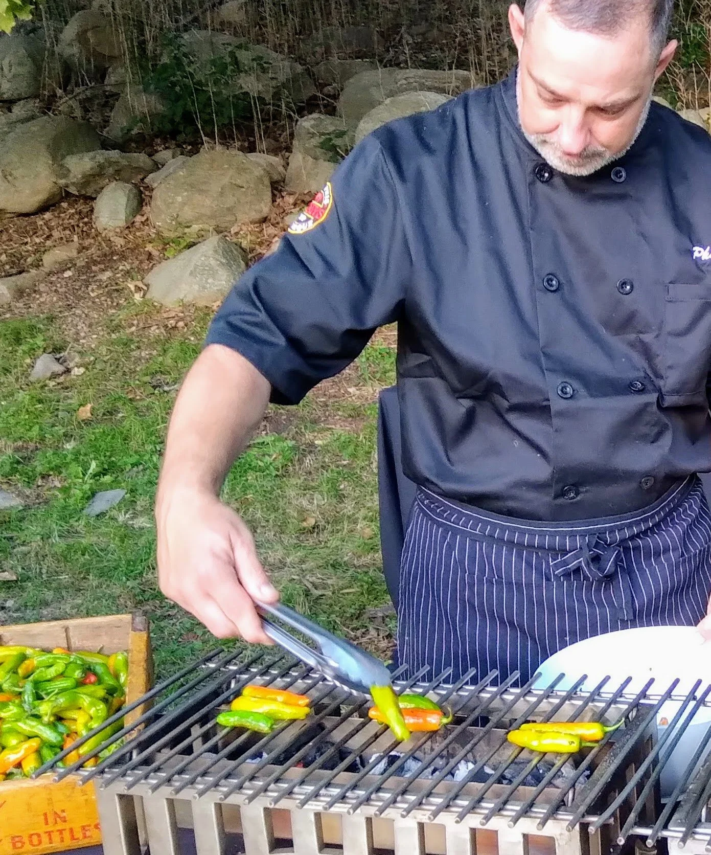 Chef grilling shishito peppers, open-fire BBQ appetizer
