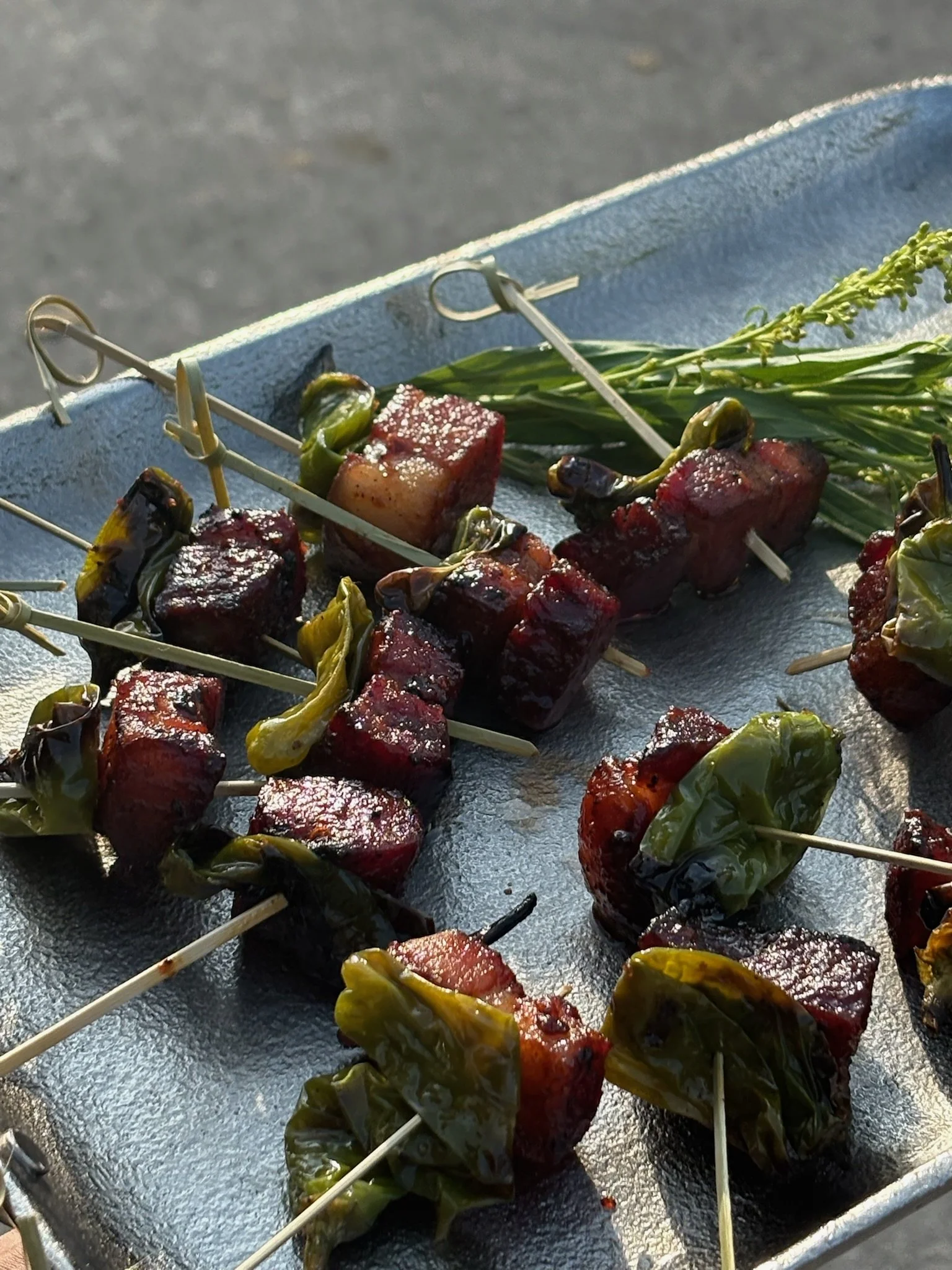 Skewers with cooked meat and grilled green peppers on a metal tray.
