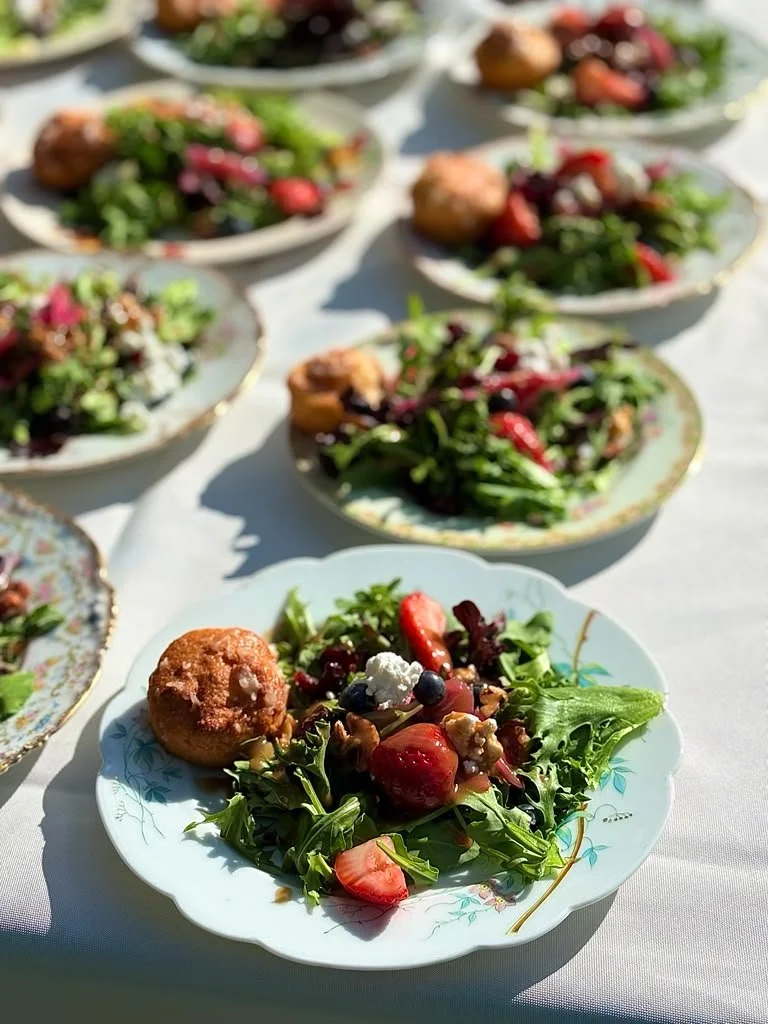 Plate with mixed salad containing strawberries, blueberries, walnuts, and a fried ball, set on a white tablecloth with several other plates of salad in the background.