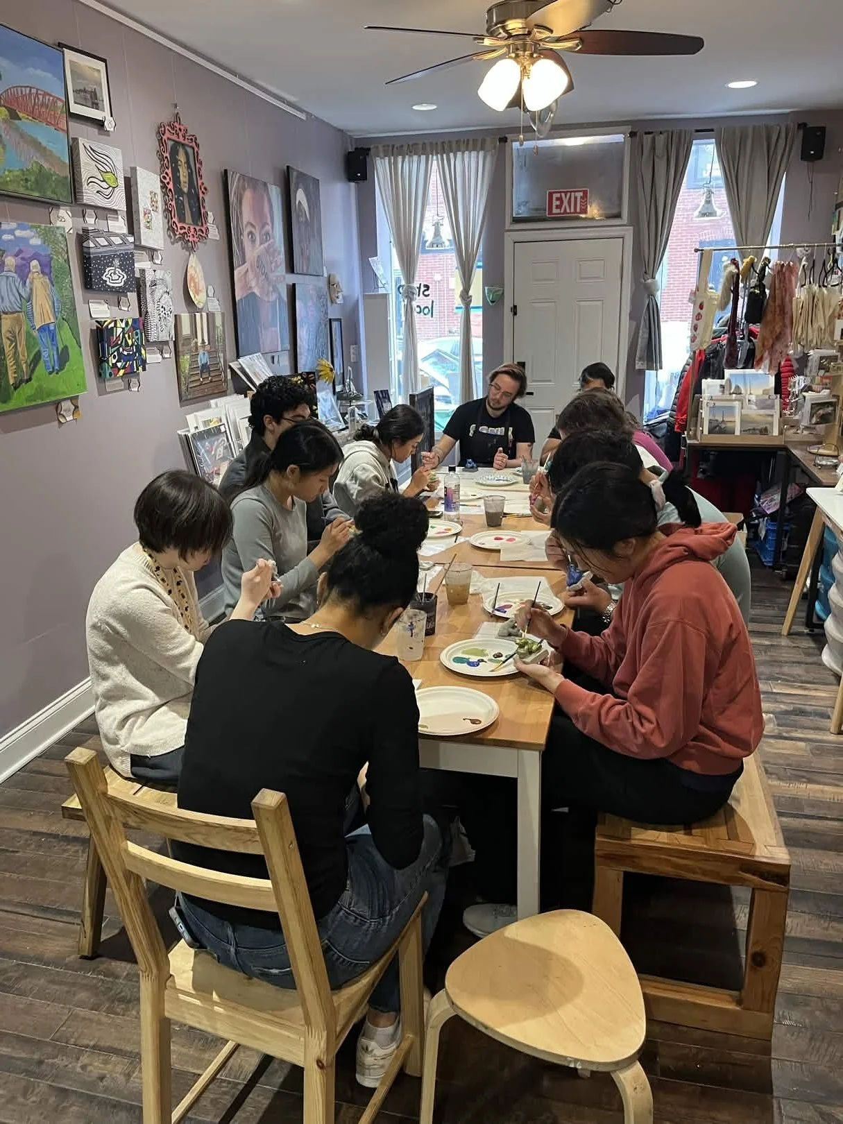 People sitting around a wooden table painting pottery in an art studio with paintings and artwork on the walls.