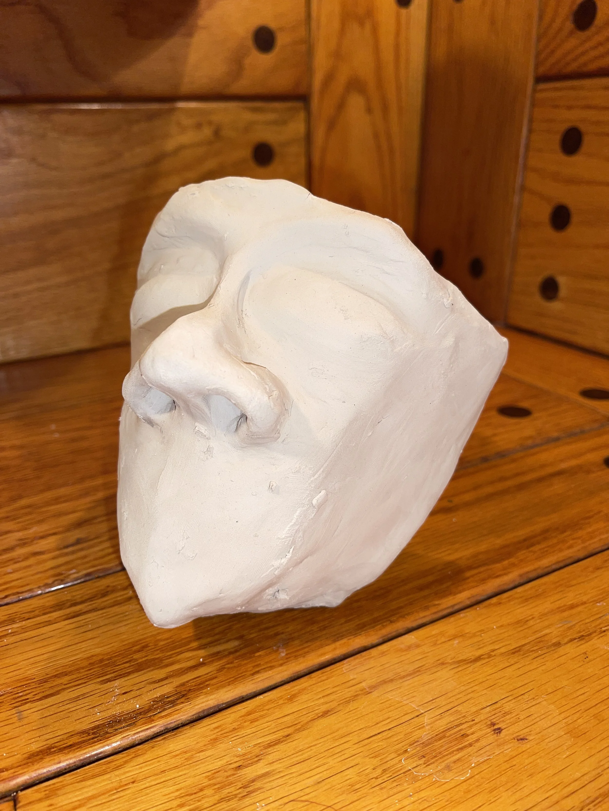 Unfinished white plaster cast of a skull placed on a wooden surface with a wooden cabinet in the background.