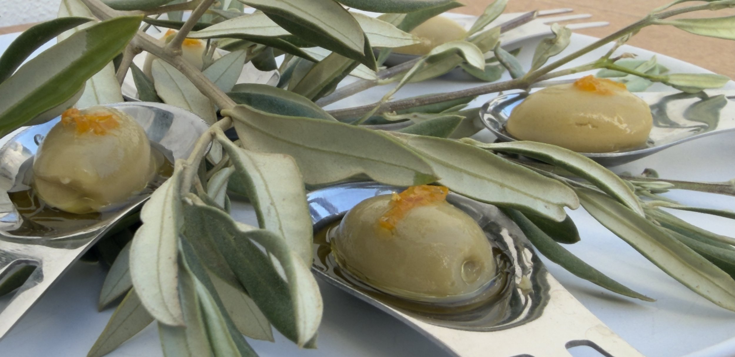Mediterranean bites: Fake Olives served on spoons among olive leaves, created by Alma Nómada.