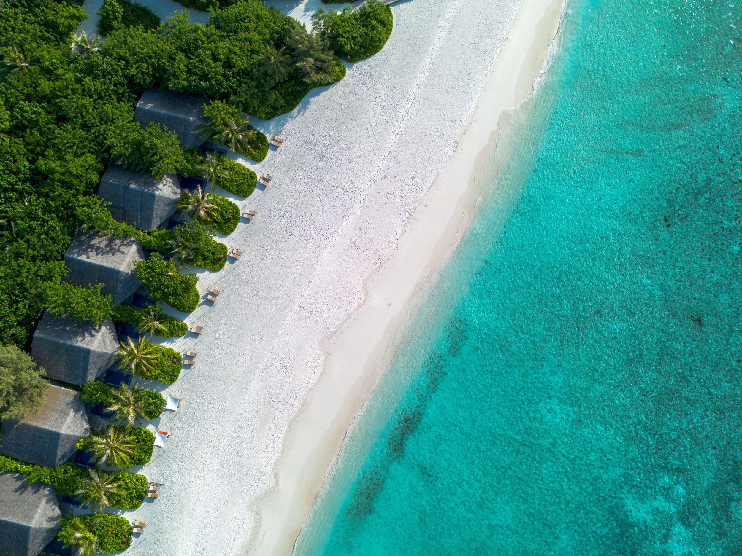Tropical island resort with private villas along a white-sand beach and turquoise sea.