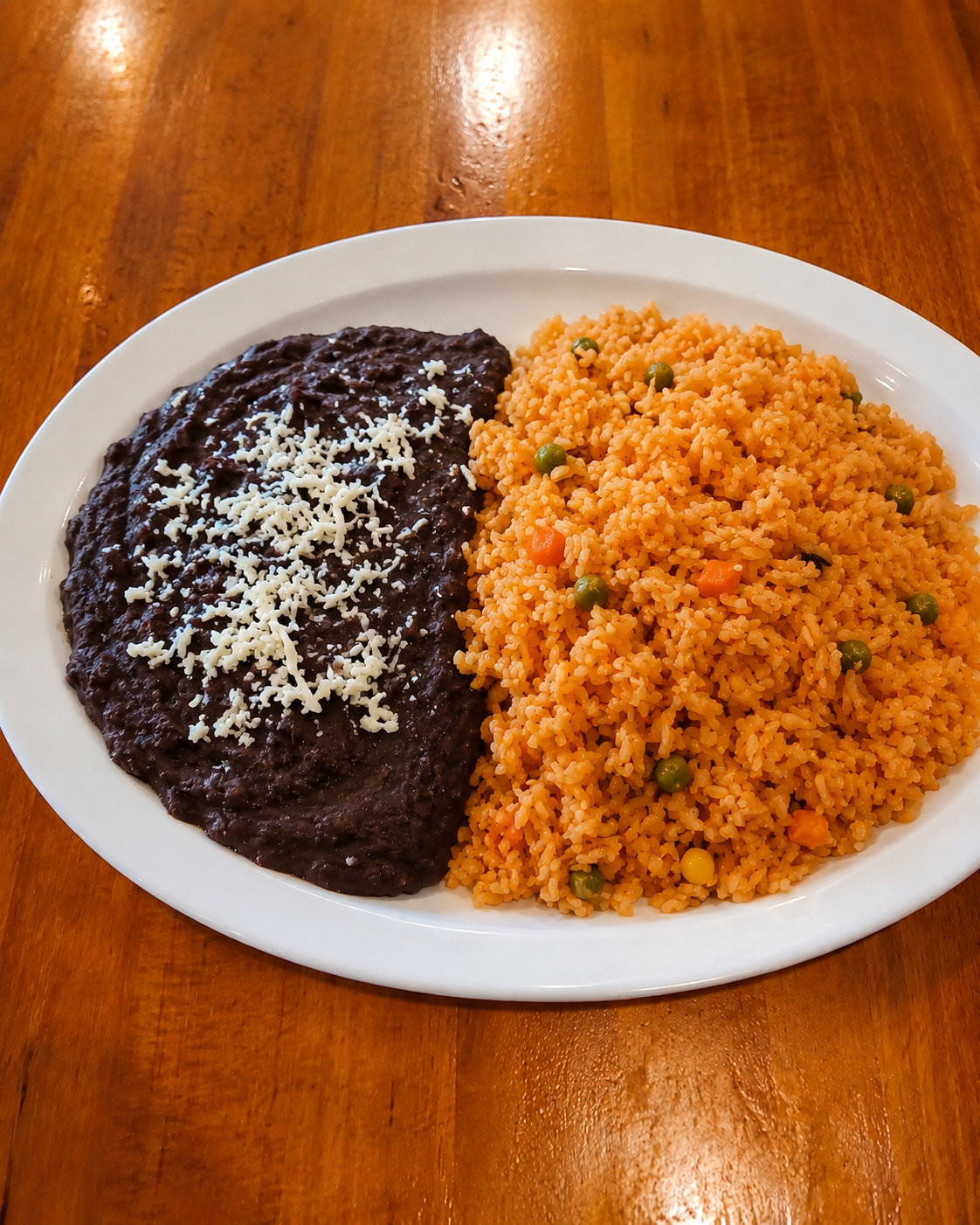 Plate with black bean burger topped with shredded cheese and a side of seasoned rice with peas and diced carrots on a wooden table.