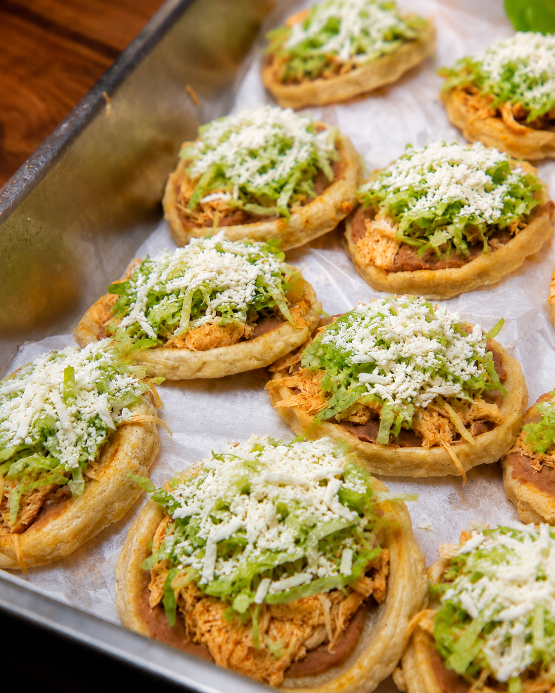 Close-up of mini taco bowls filled with shredded chicken, shredded lettuce, and grated cheese, arranged on a tray lined with parchment paper.