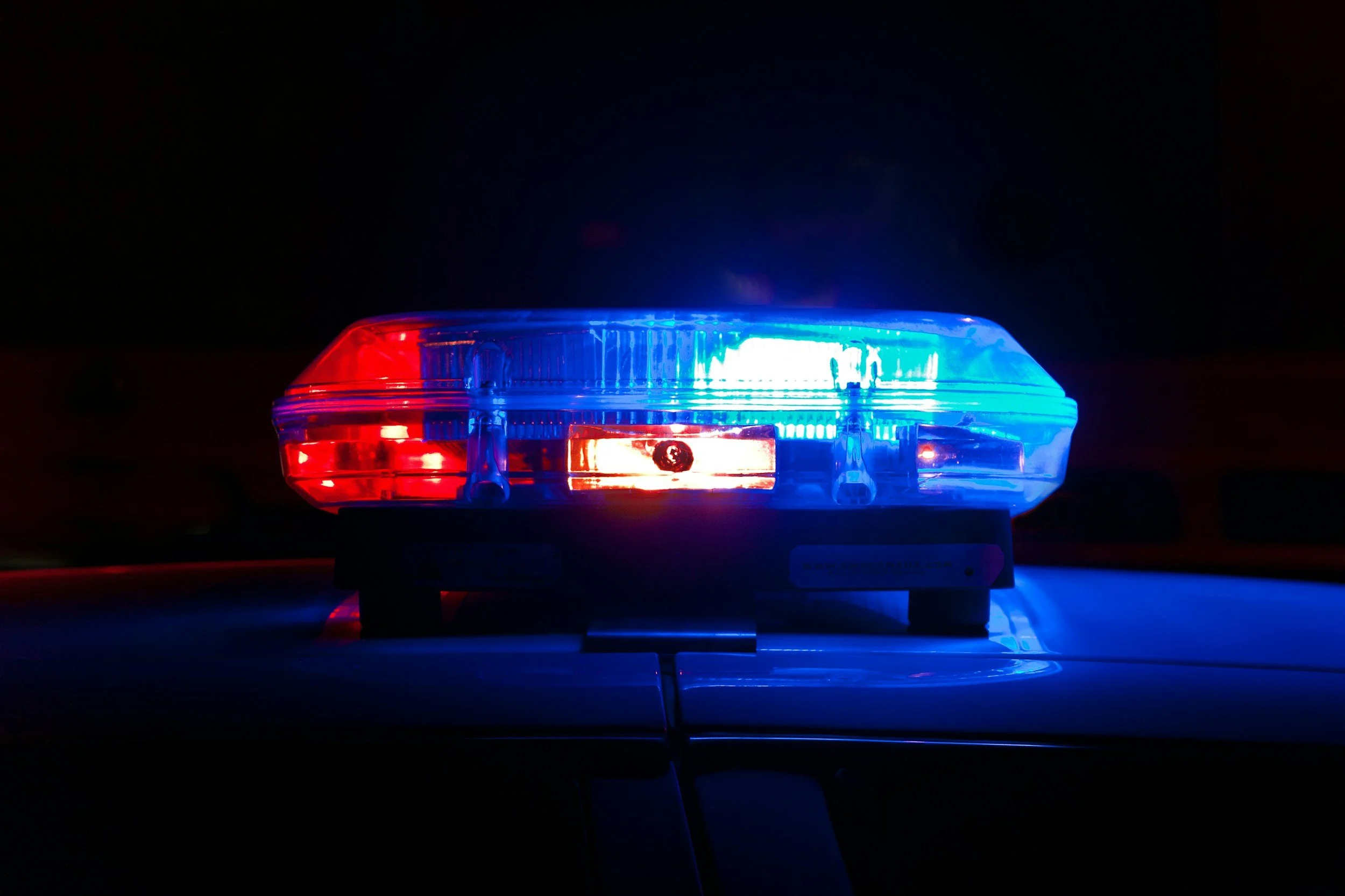 A police car light bar flashing red and blue lights in the dark.