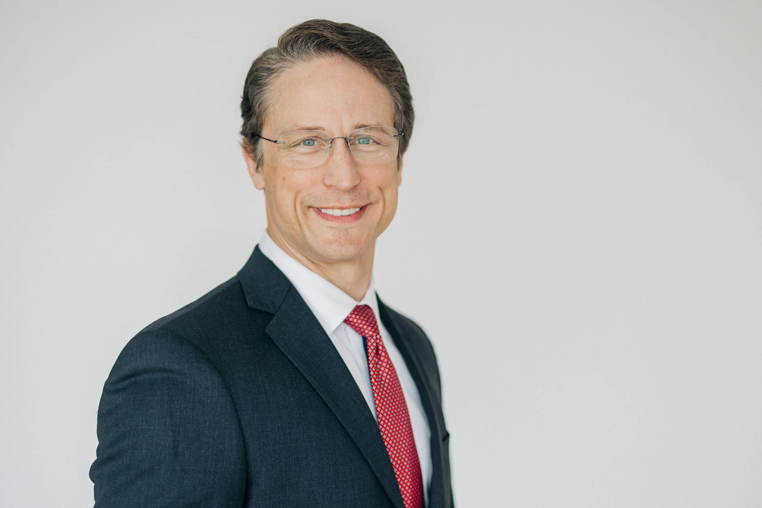 A smiling man in a blue suit and tie posing with arms crossed in front of a plain background.
