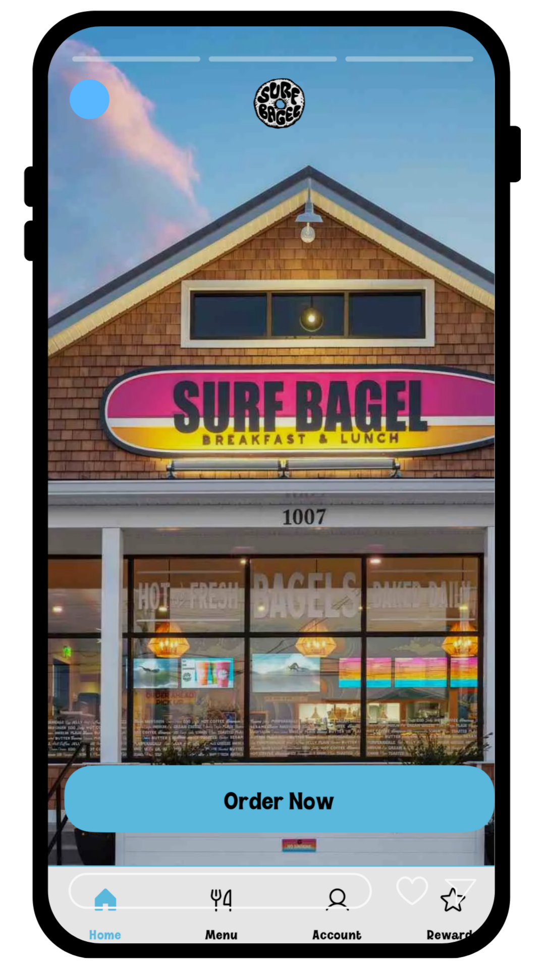 Front view of a restaurant named 'Surf Bagel' offering breakfast and lunch, with large window displaying interior and colorful neon signs, located at 1007.