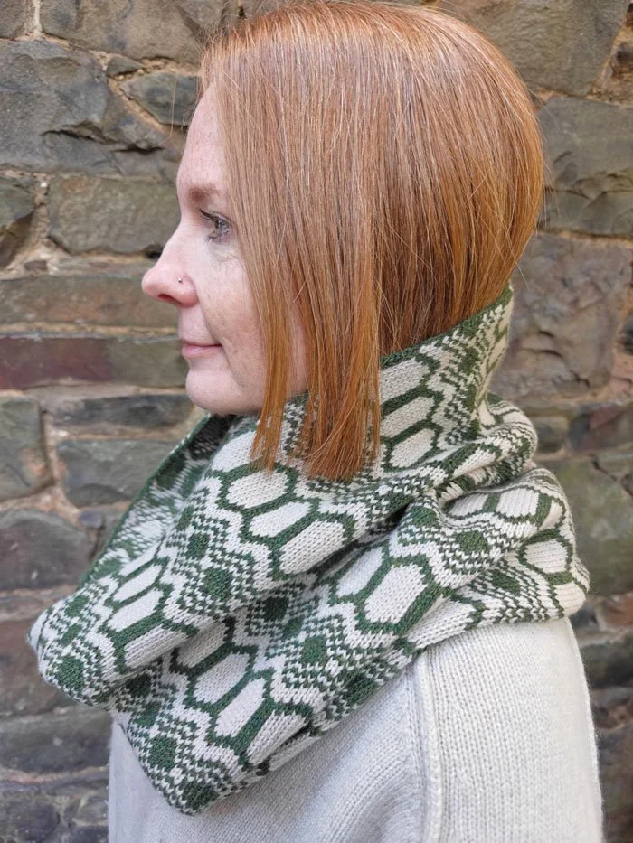 100% Wool Strandhill snood in moss green and light stone colourway. Modelled by a young woman with red hair and photographed against a textured brick wall