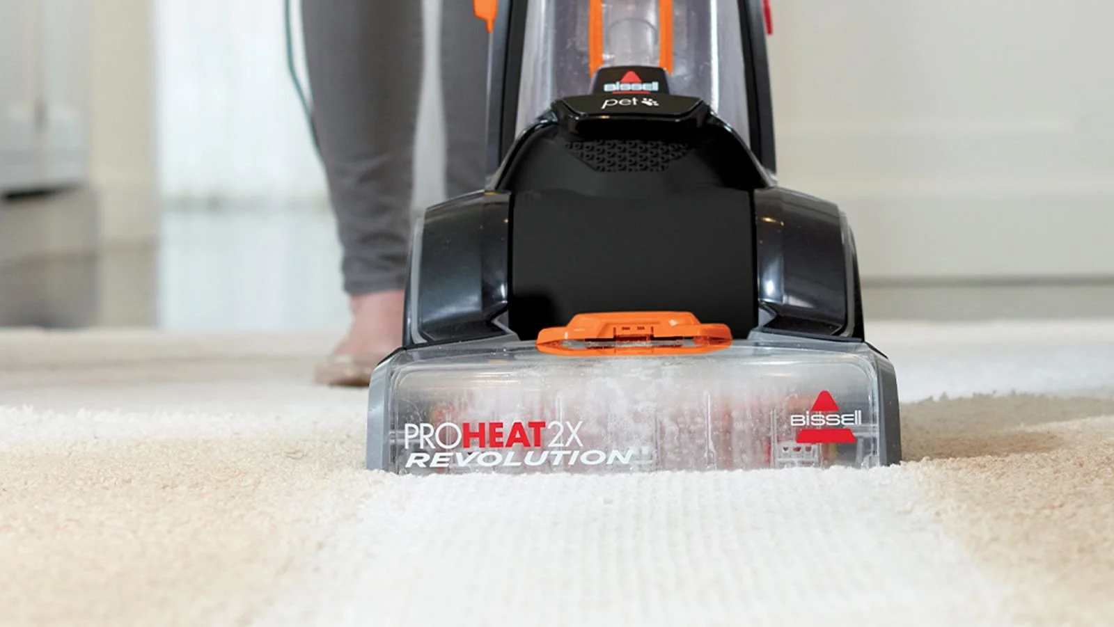 A person using a Bissell ProHeat 2X Revolution carpet cleaner to clean a beige carpet.