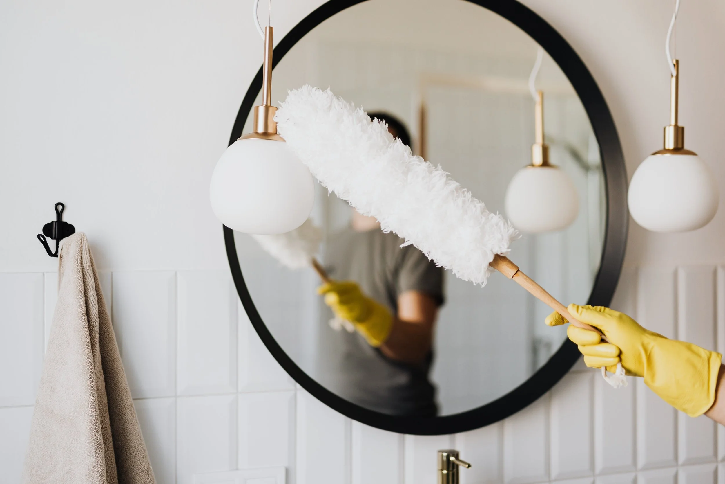 Person cleaning a mirror with a white duster in a modern bathroom with hanging light fixtures