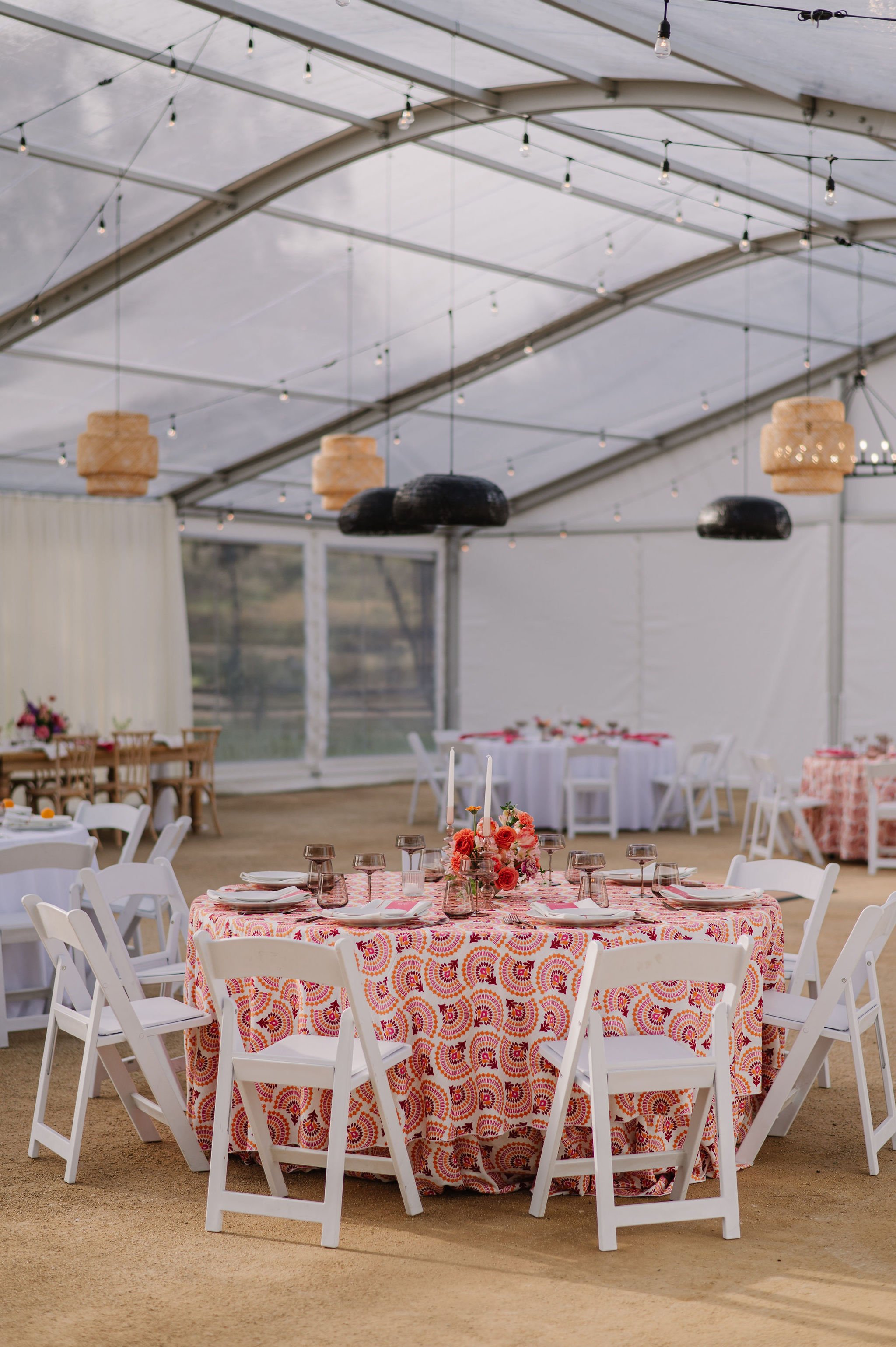 Table with a bold printed red tablecloth and colorful flowers surrounded by white chairs inside Tar Creek Ranch's Magnolia Pavilion for their summer/spring gala styled shoot event