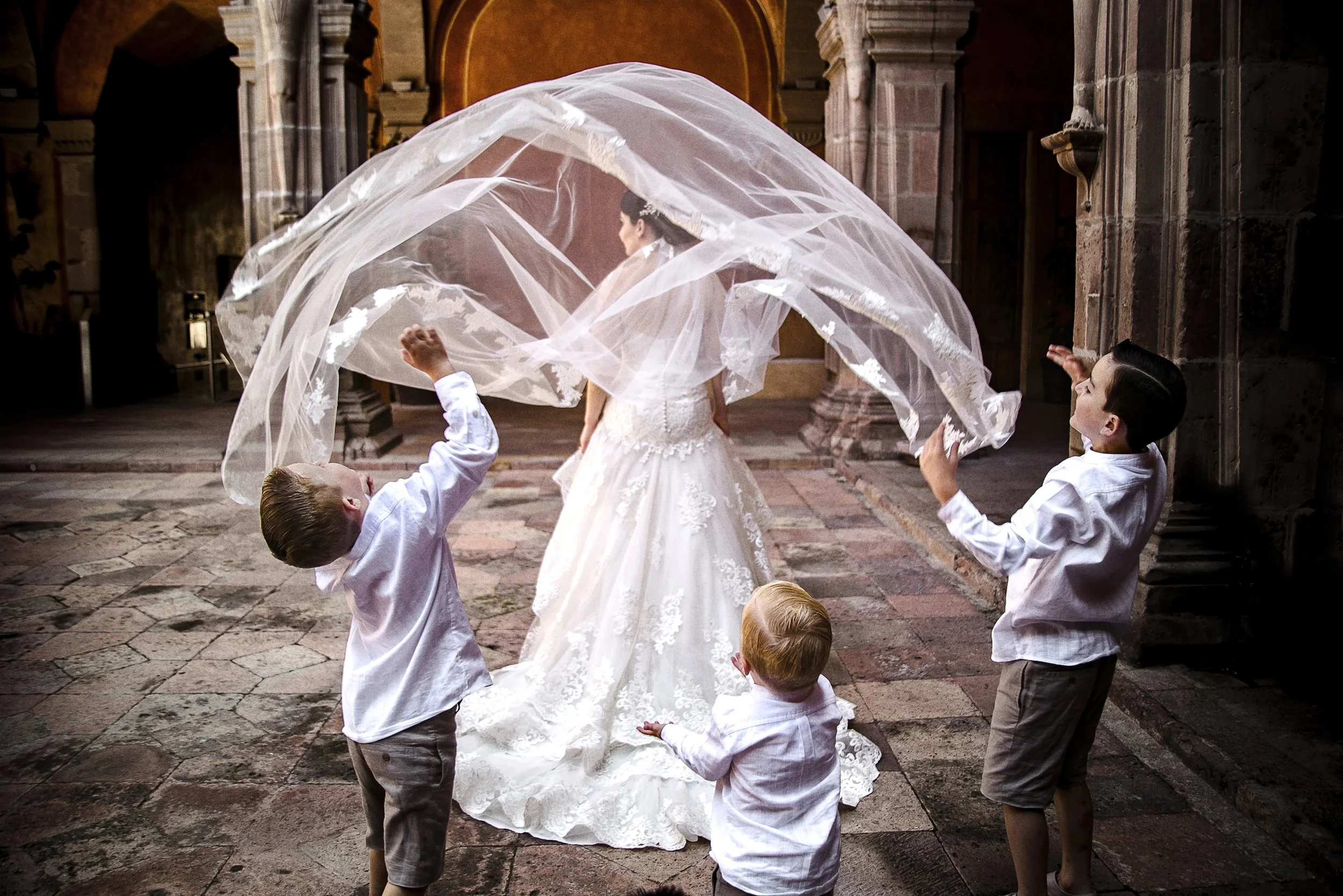 Fotografía documental de niños jugando con el velo de la novia en exterior, movimiento y gesto espontáneo.