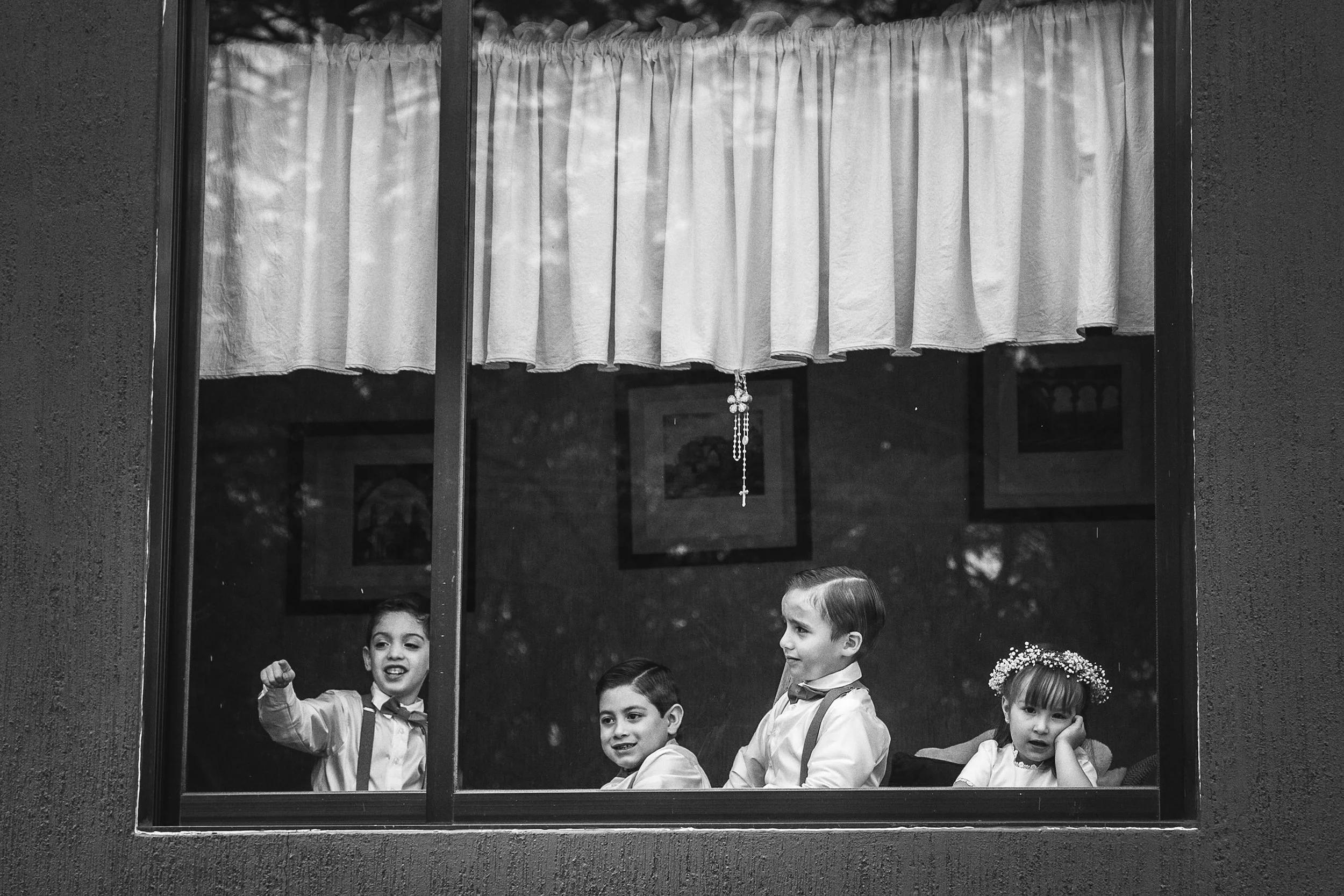 Fotografía en blanco y negro de niños observando la ceremonia desde una ventana.