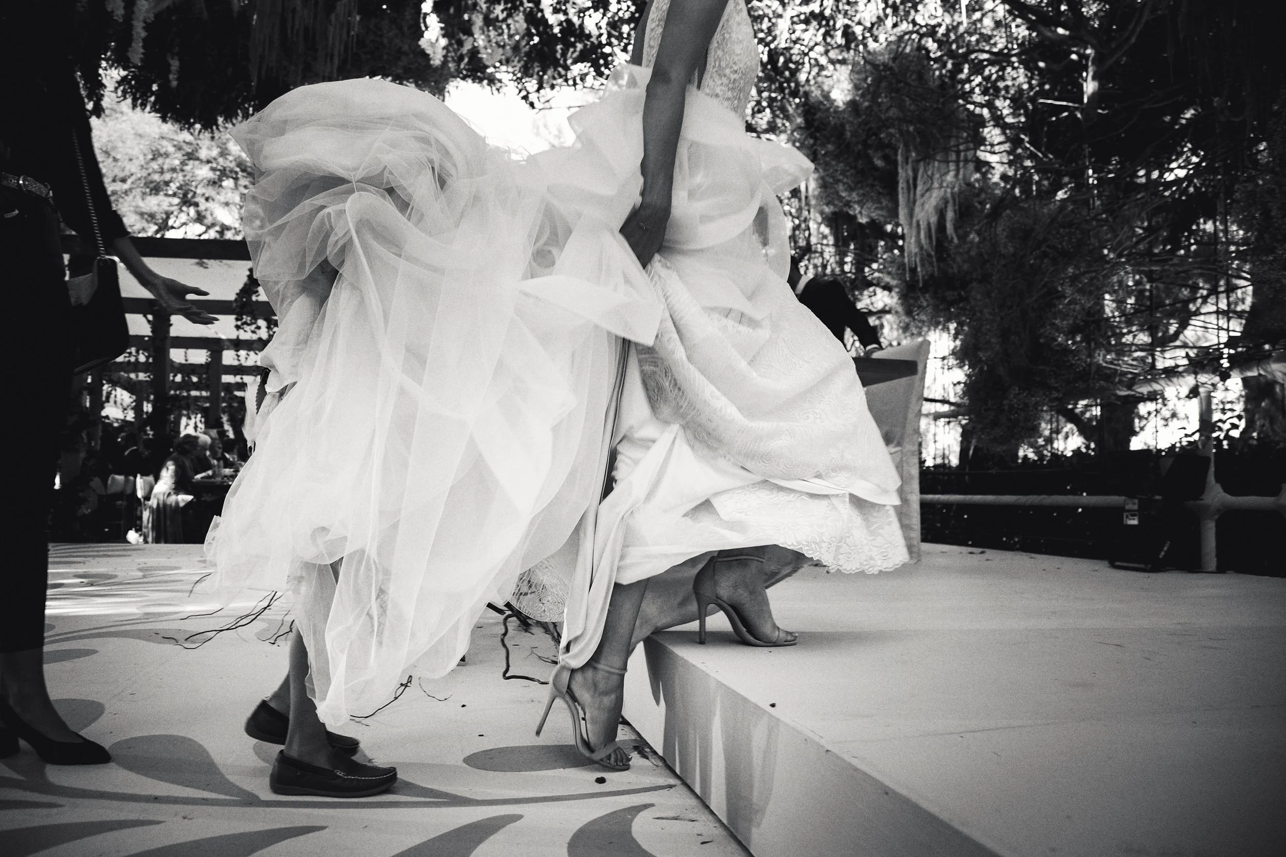 Fotografía en blanco y negro de novia levantando vestido al subir escalones, gesto dinámico.