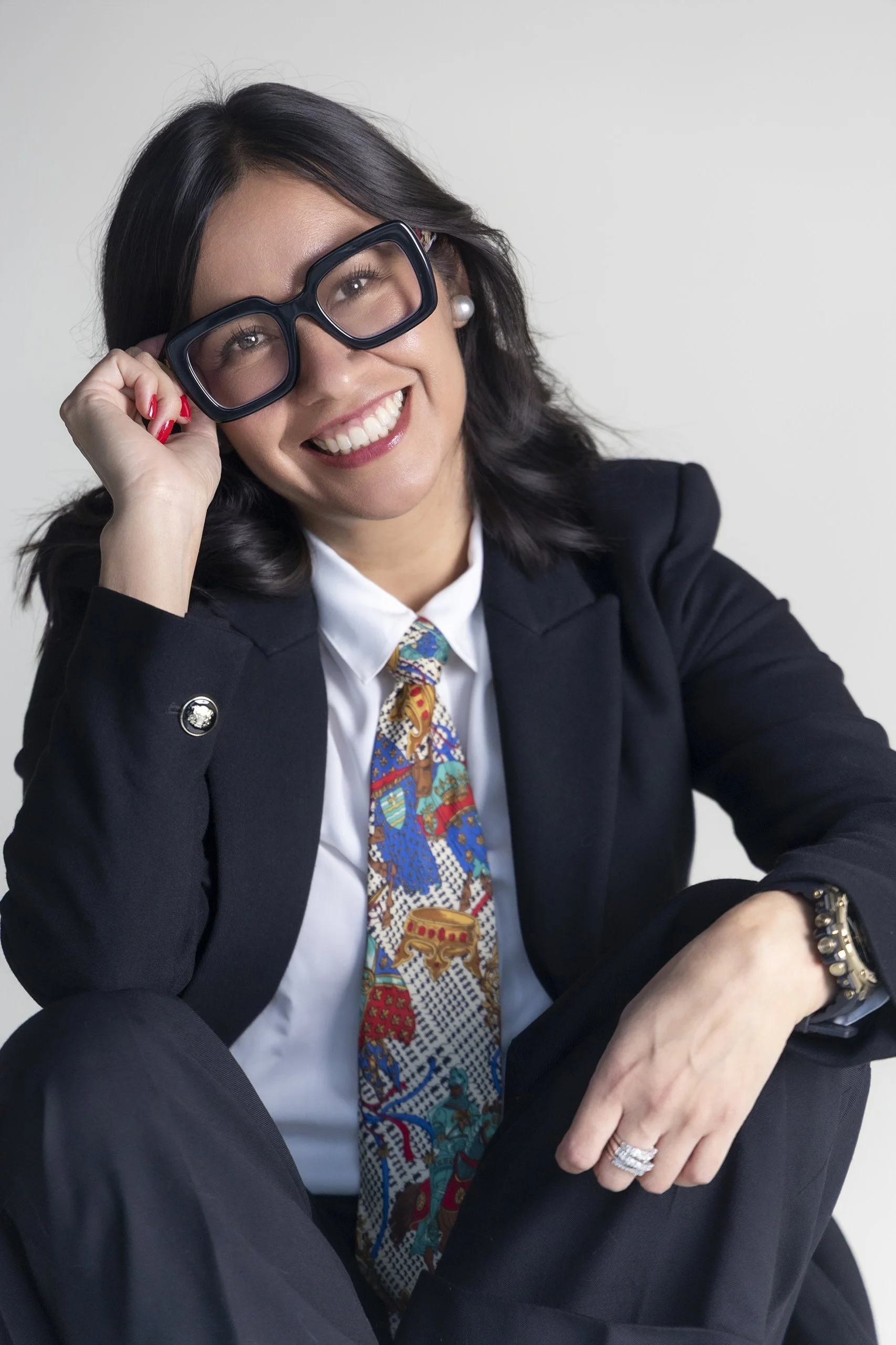 Retrato de mujer con traje formal y lentes, sonrisa amplia y presencia segura en estudio.