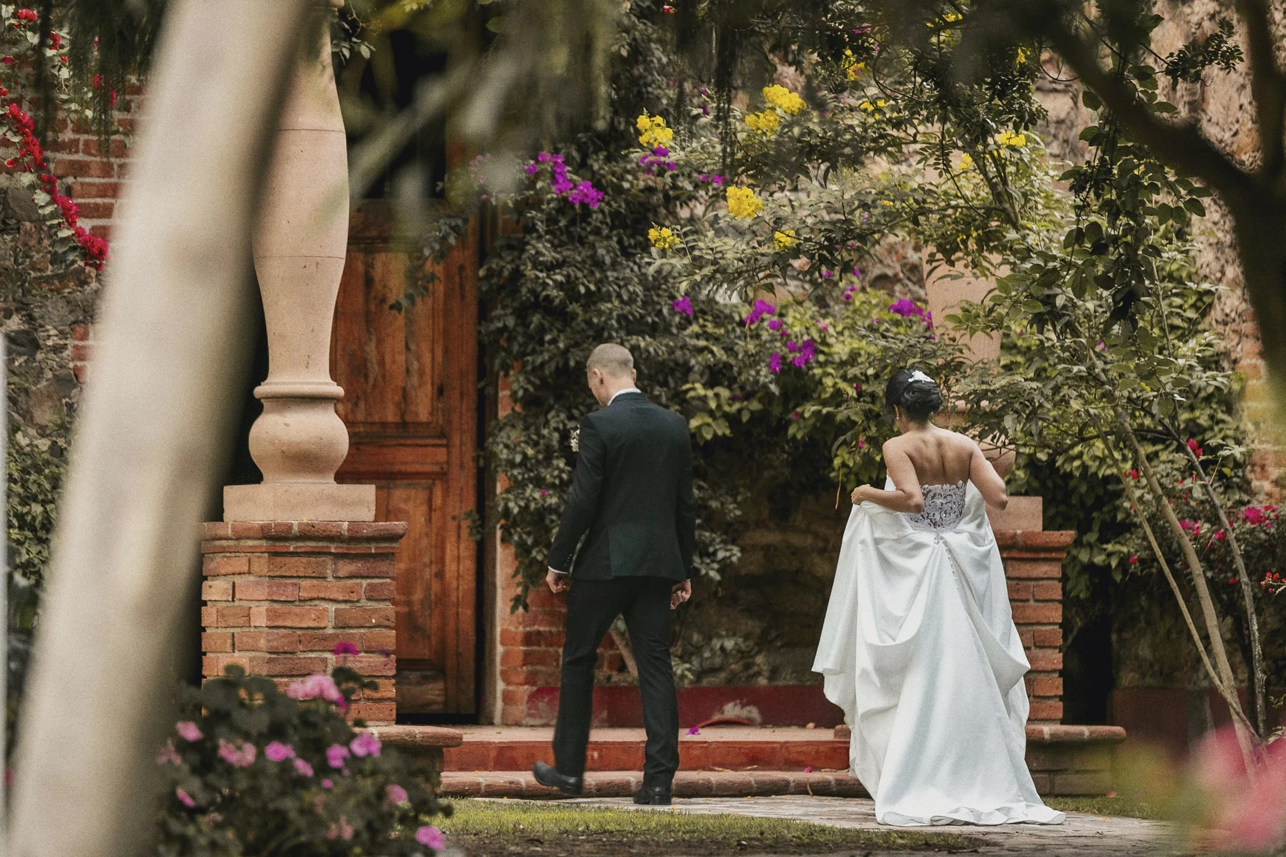 Fotografía de novios caminando entre arcos y vegetación del lugar de la ceremonia.