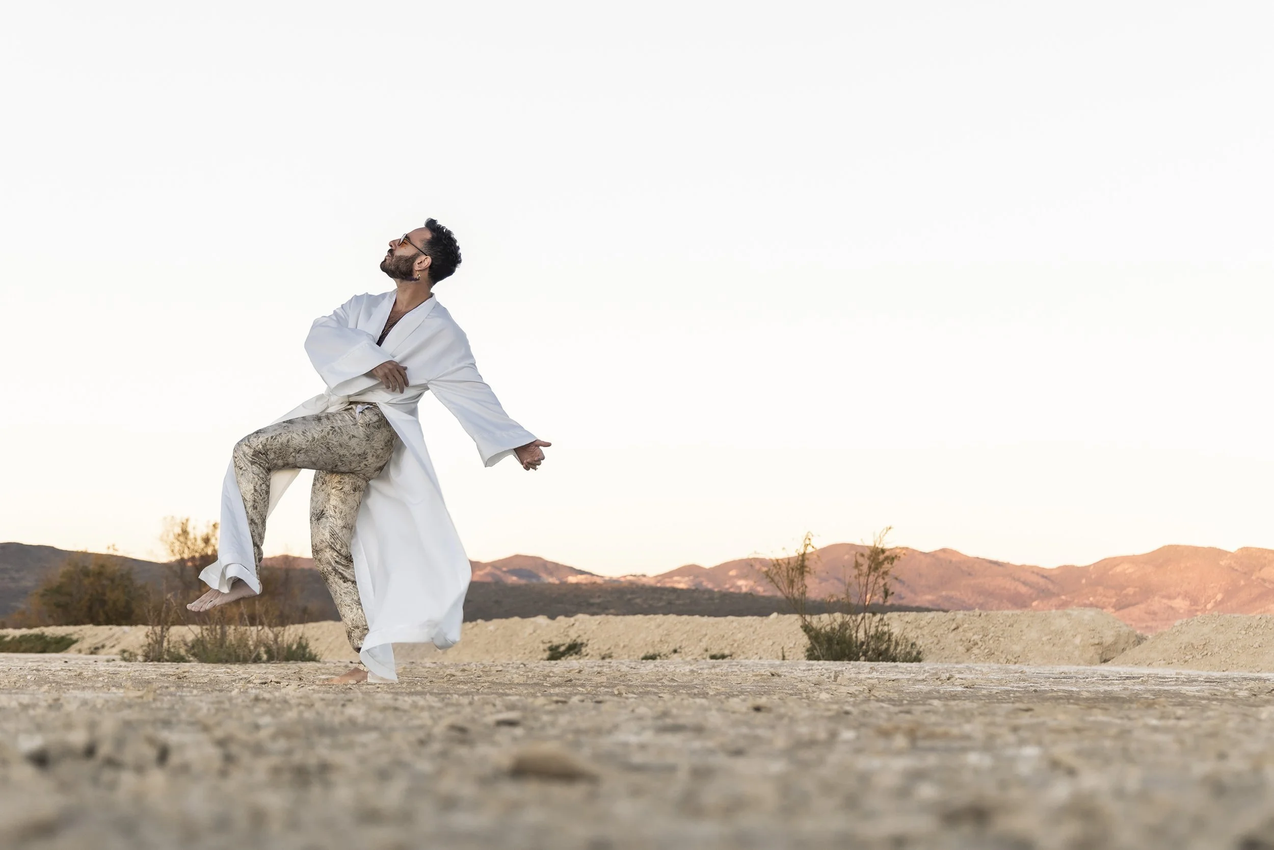 Retrato de hombre en exterior desértico, cuerpo en movimiento y expresión libre, luz natural.