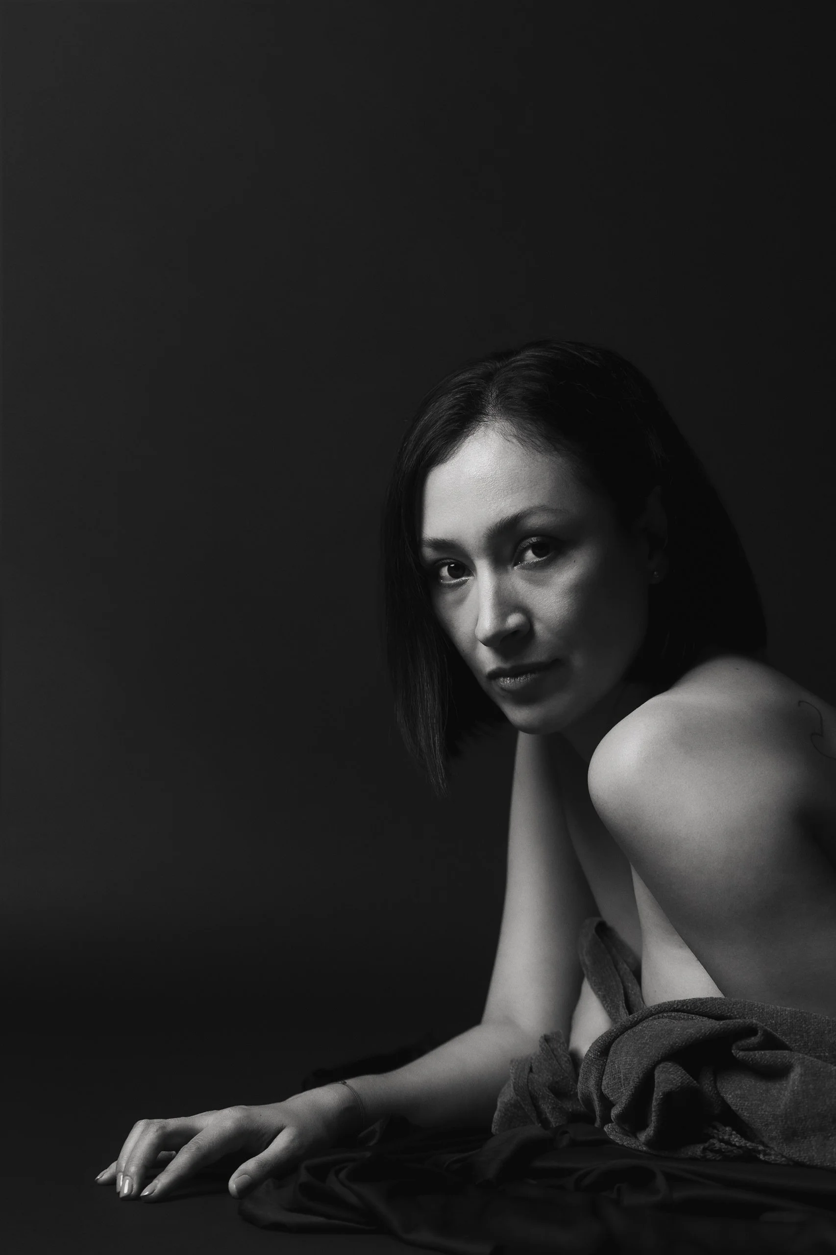 Retrato artístico de mujer en estudio con luz dramática, hombros descubiertos y mirada directa.