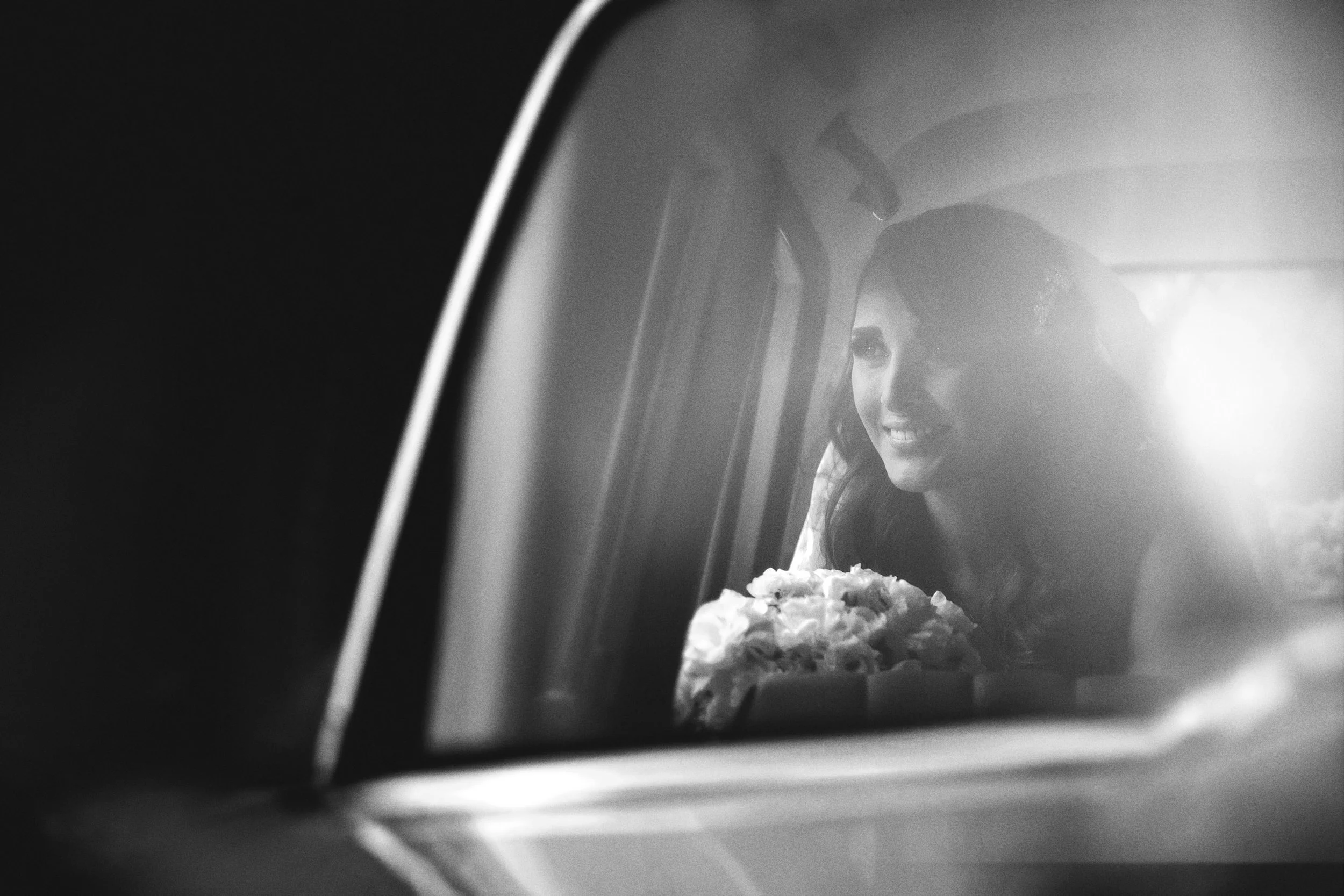 Fotografía en blanco y negro de novia reflejada en la ventana de un automóvil, mirada serena.