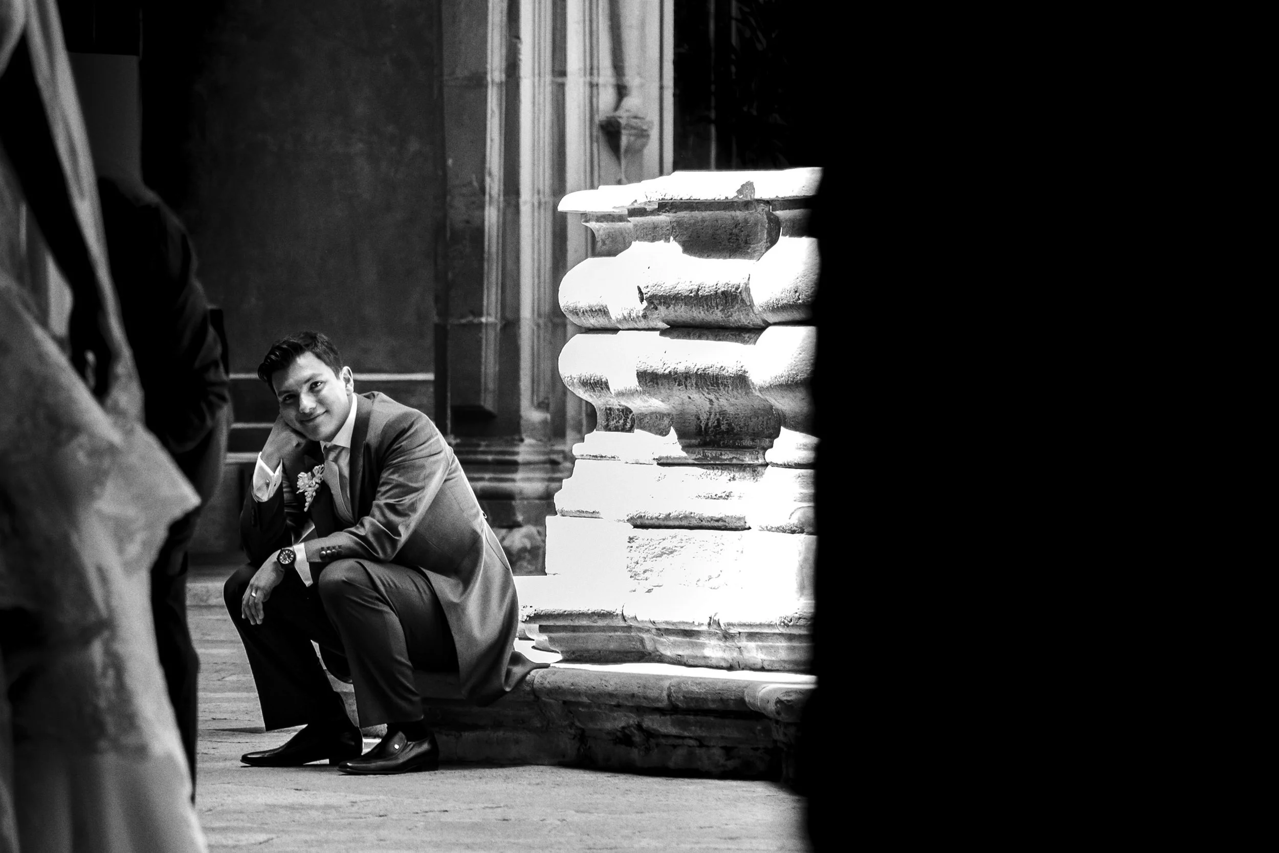 Fotografía en blanco y negro de novio sentado en escalinata exterior, momento de pausa y espera.