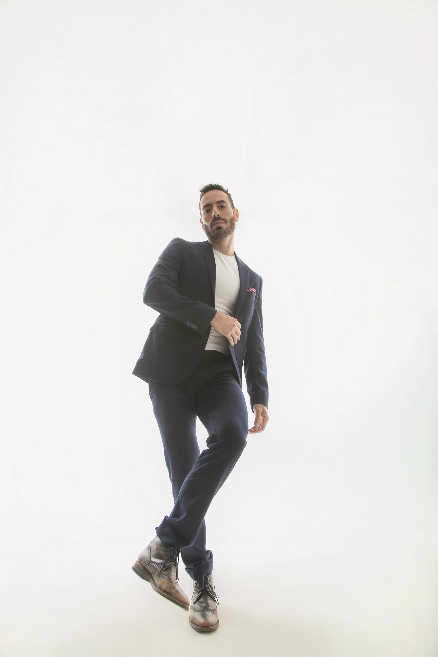 Retrato de hombre caminando en estudio con traje oscuro, fondo claro y postura segura.