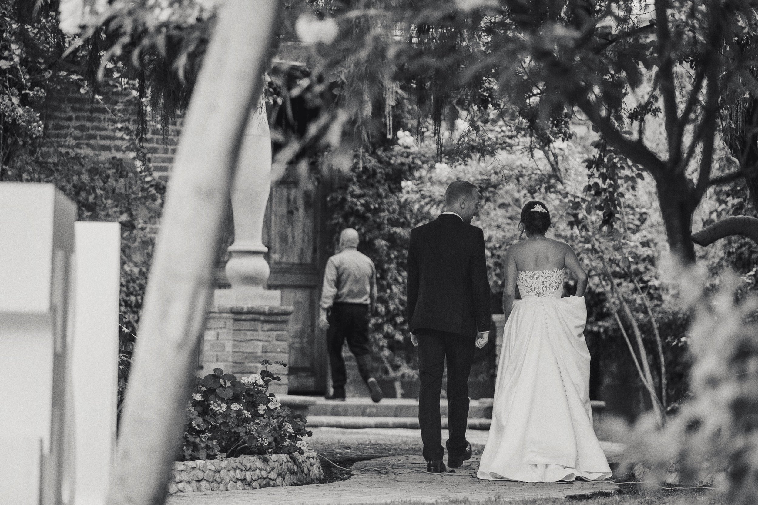 Fotografía en blanco y negro de novios caminando de espaldas en jardín.