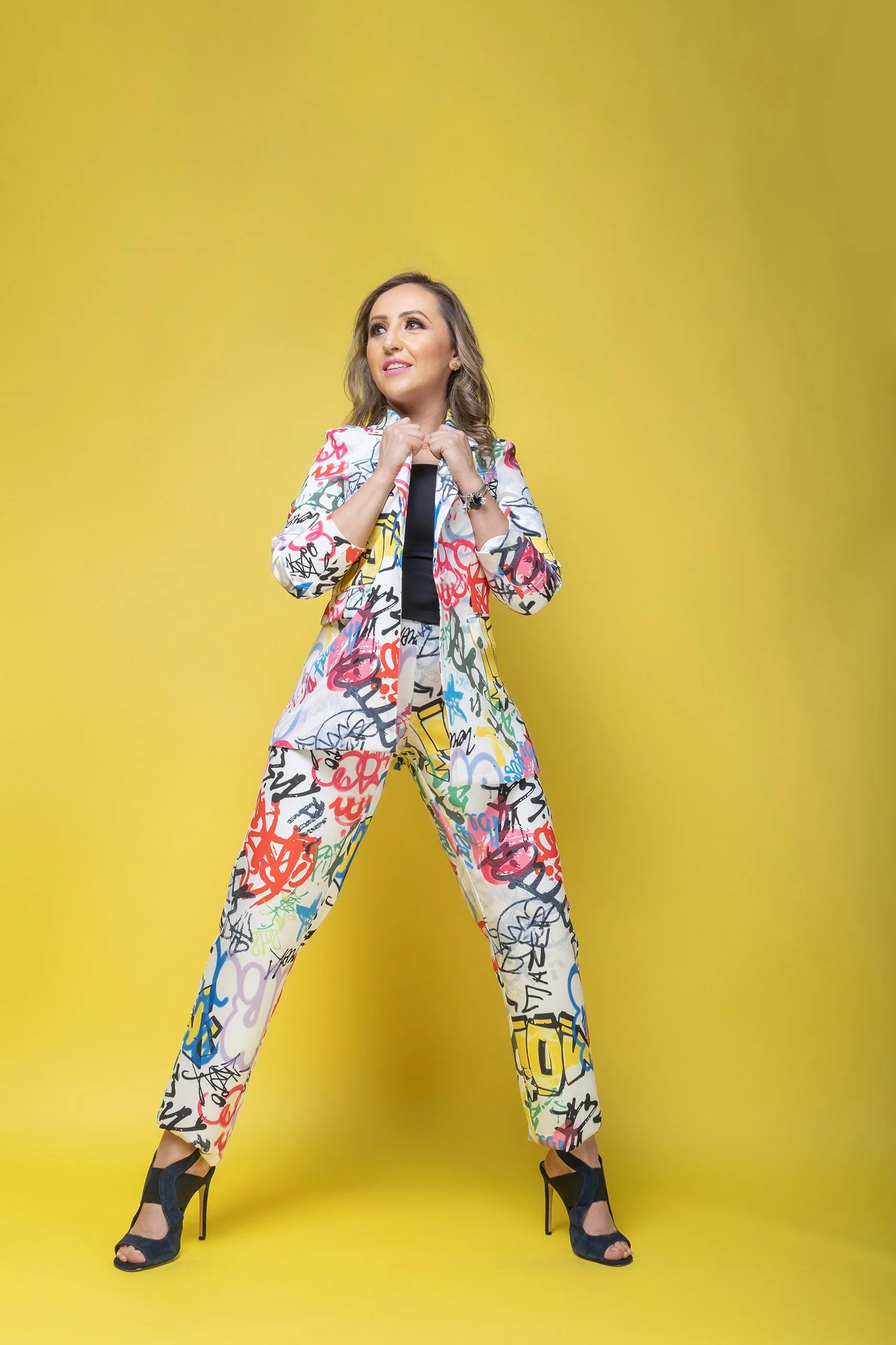 Retrato de mujer en estudio con fondo amarillo, vestimenta colorida y postura erguida.