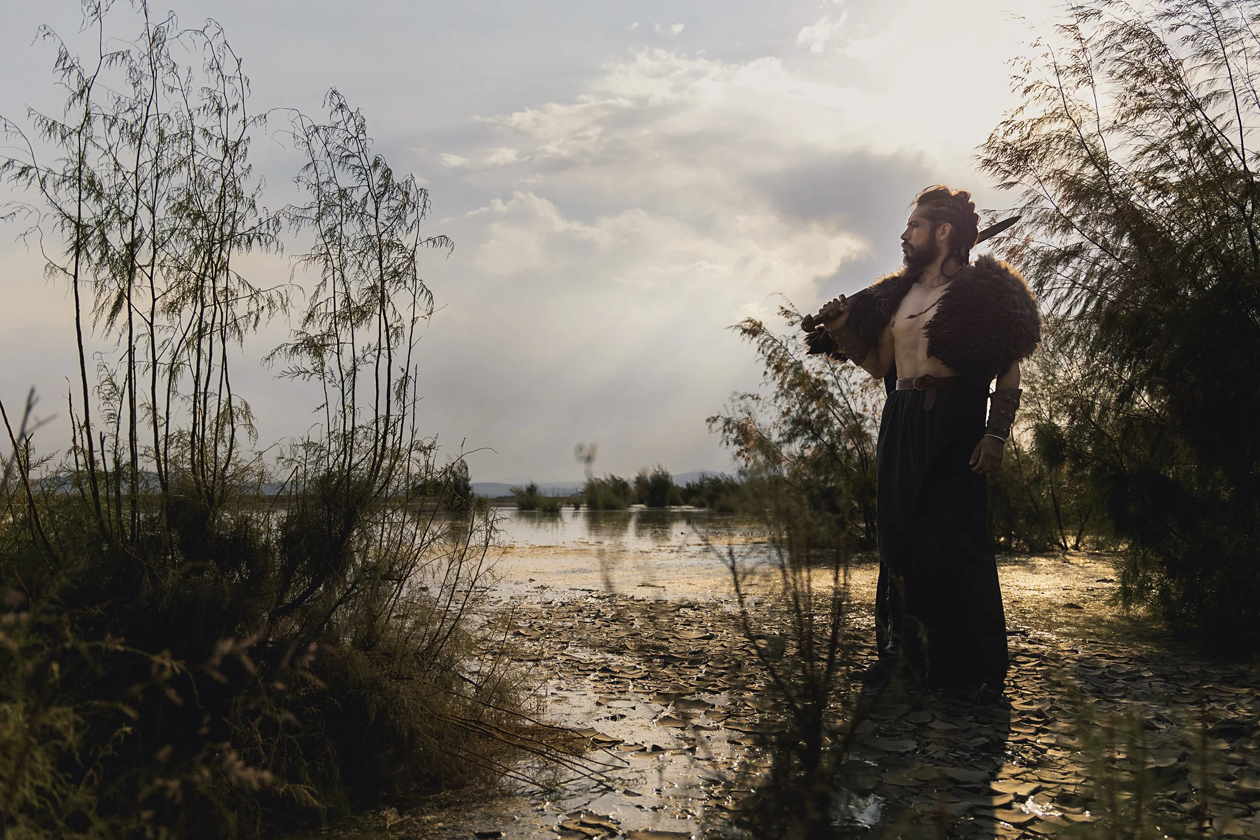 Retrato de hombre en exterior al atardecer, de pie junto al agua, atmósfera silenciosa y natural.