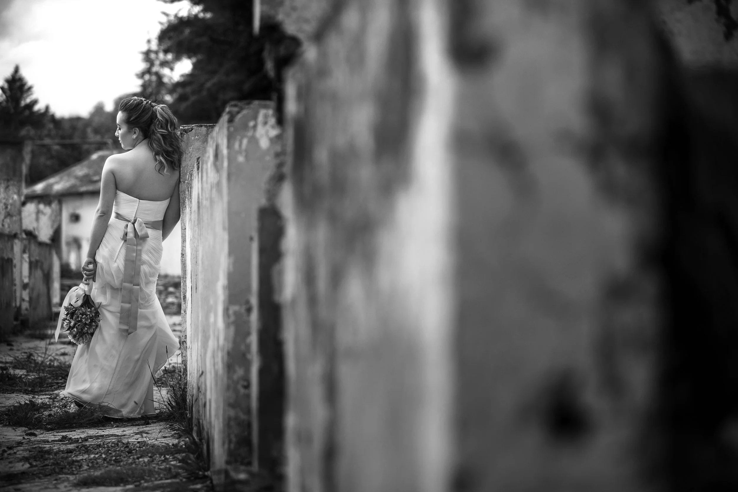 Fotografía en blanco y negro de novia vista parcialmente tras muro, momento íntimo previo.