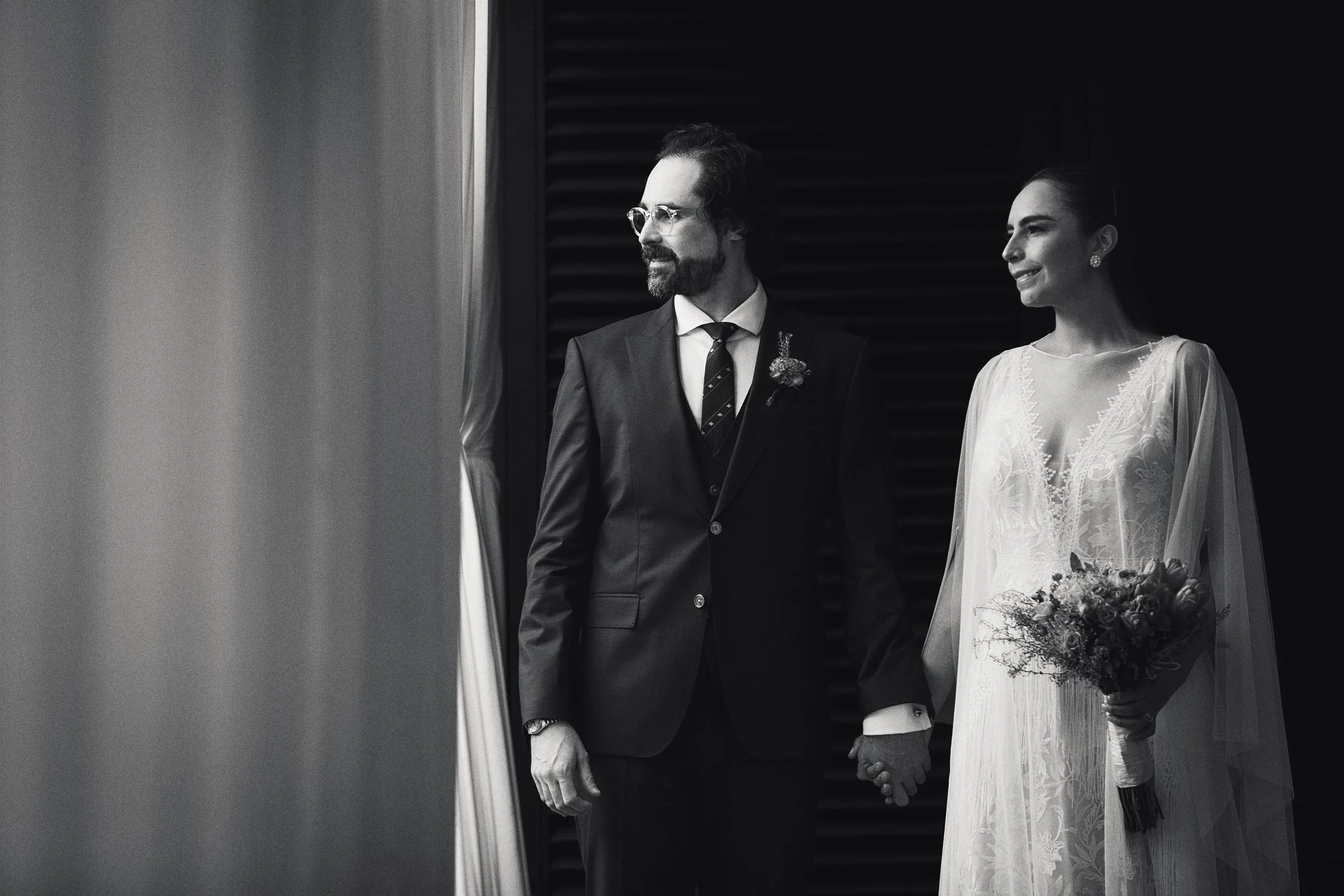 Fotografía en blanco y negro de novios tomados de la mano al salir de ceremonia.