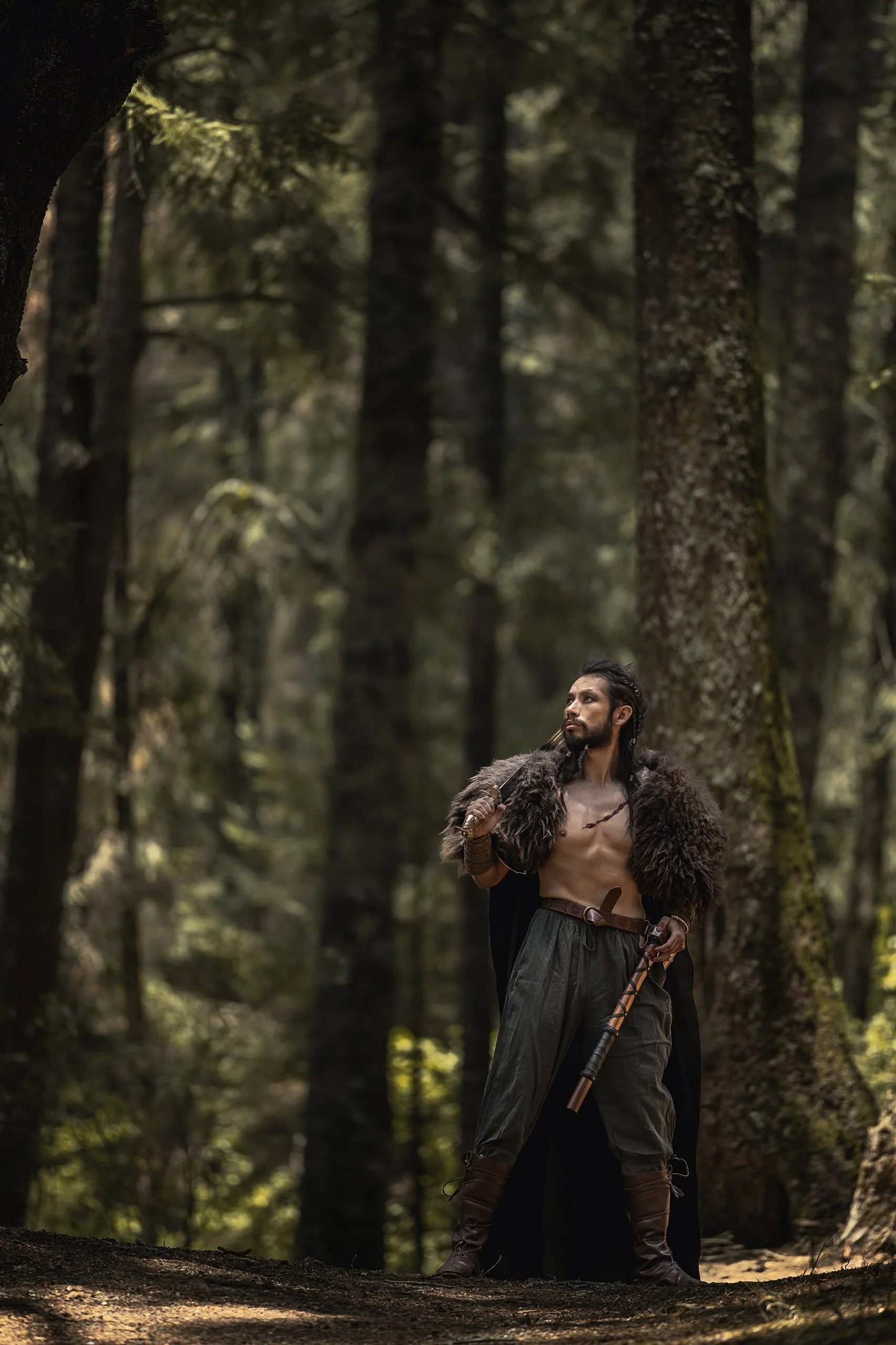 Retrato de hombre en bosque, torso descubierto y vestimenta ritual, postura firme entre árboles.