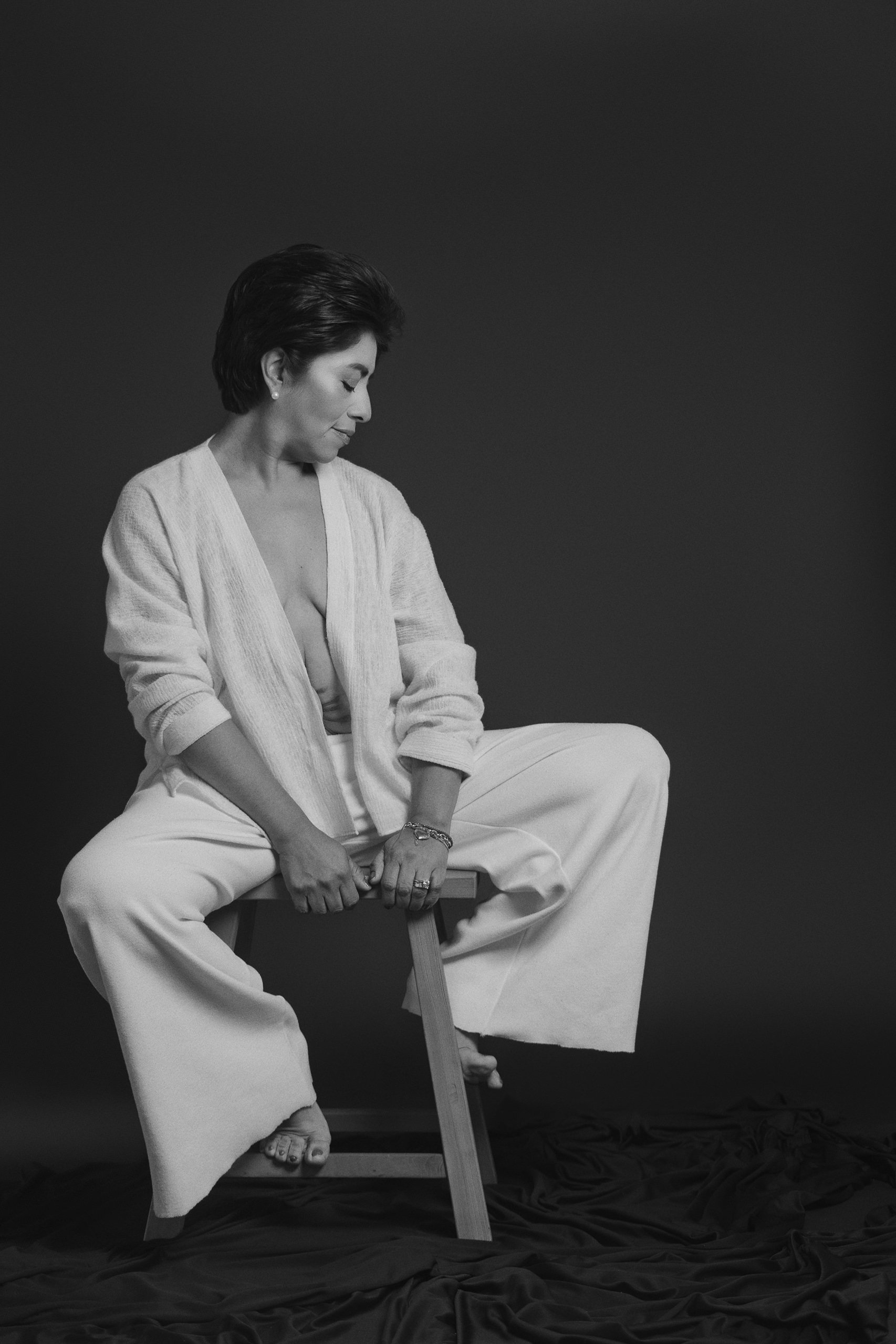 Retrato en blanco y negro de mujer sentada en banco, vestimenta clara y expresión introspectiva.