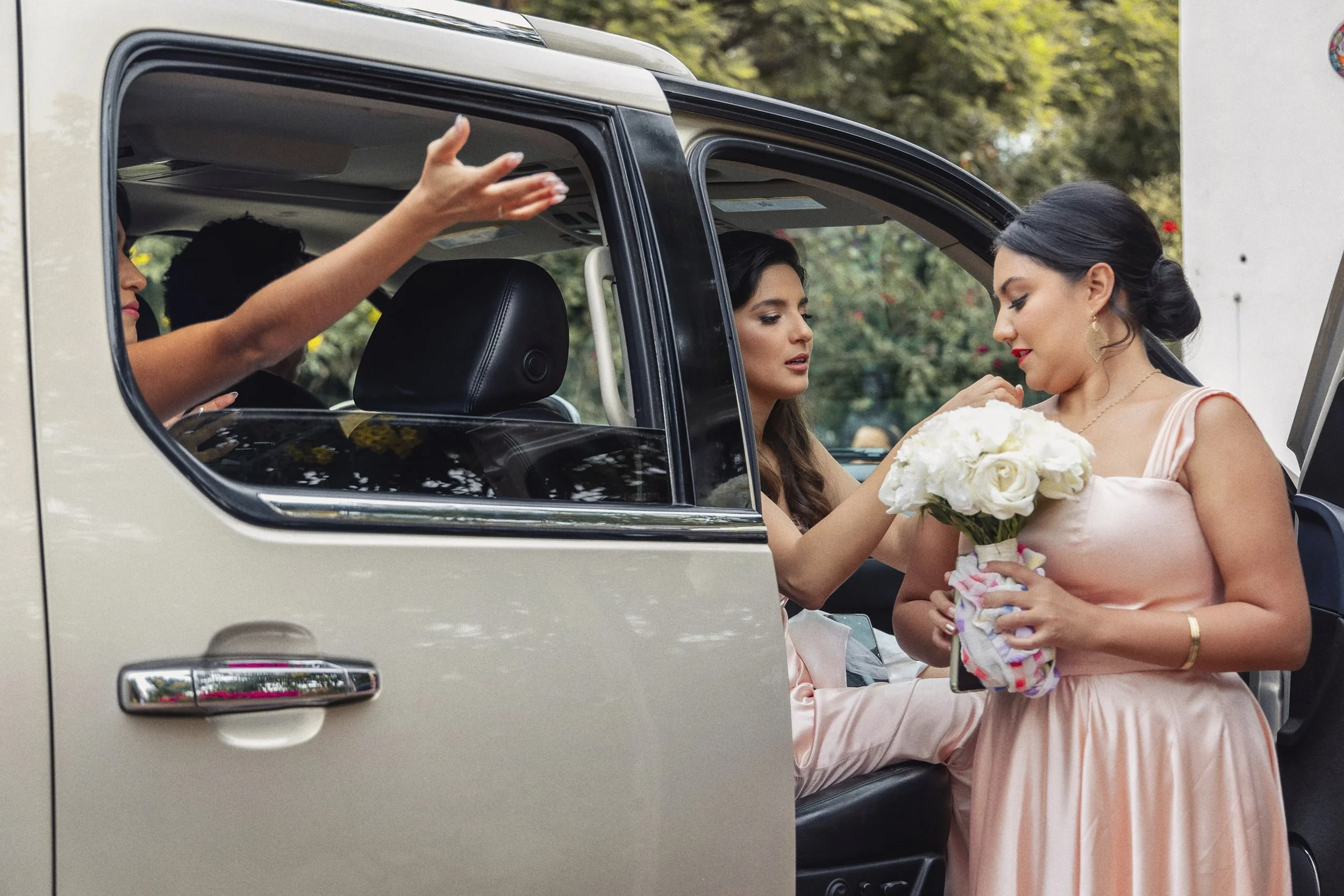 Fotografía documental de novia dentro de automóvil recibiendo flores y despedida previa.