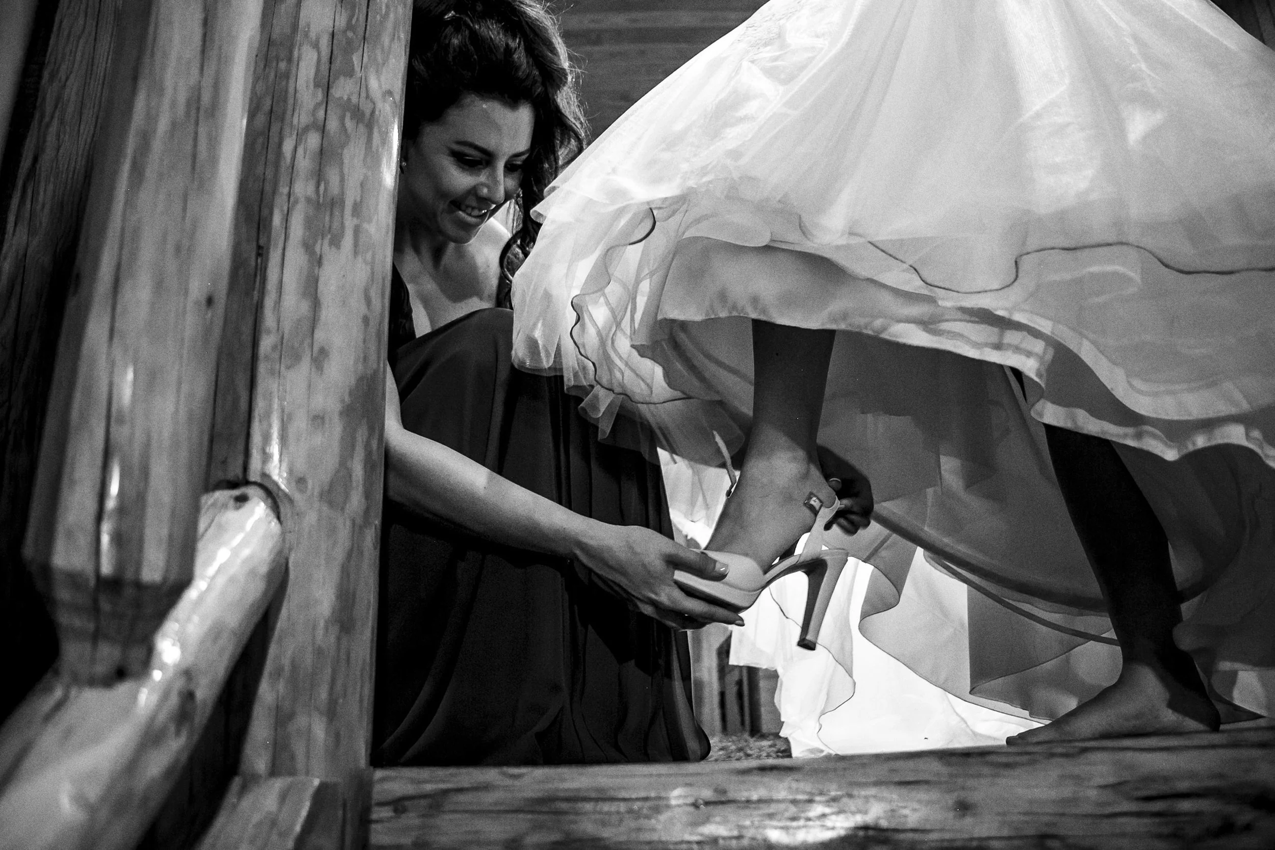 Fotografía en blanco y negro de mujer ayudando a novia a ajustar zapato, momento íntimo.