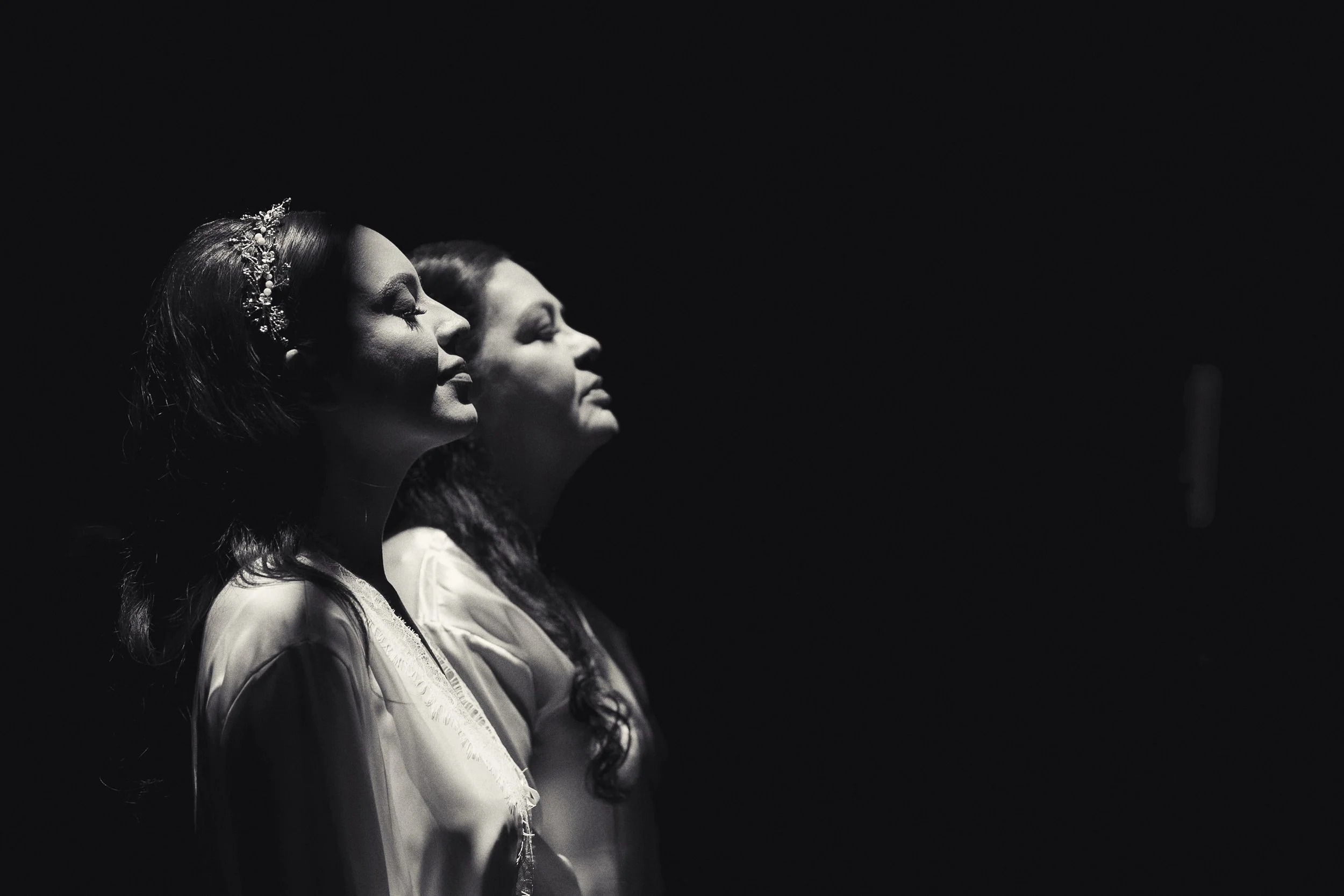 Fotografía en blanco y negro de novia mirando hacia arriba, perfil iluminado y gesto emotivo.