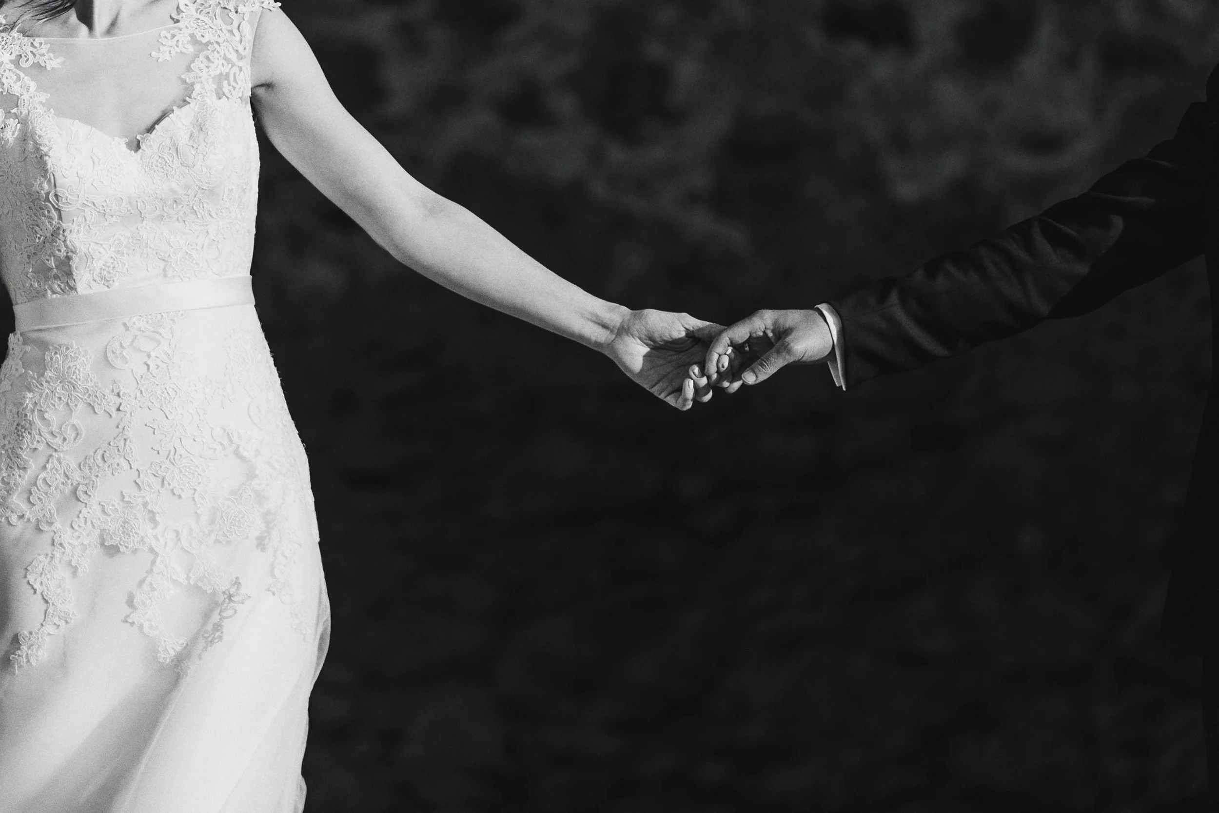 Fotografía en blanco y negro de novios tomados de la mano, detalle de manos entrelazadas.