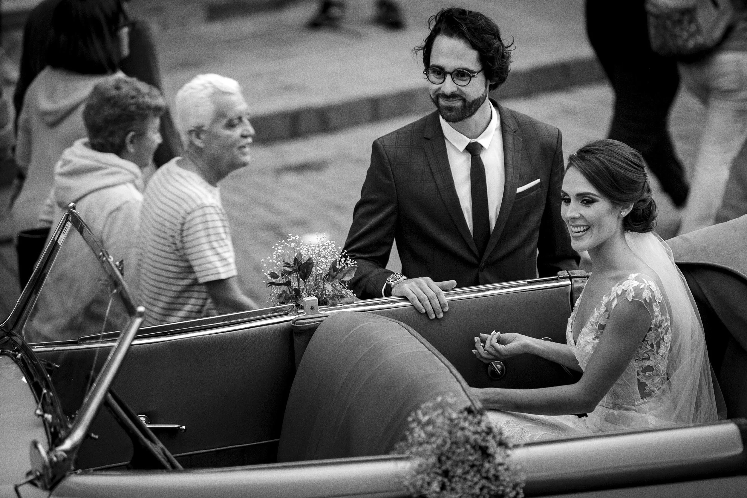Fotografía en blanco y negro de novios sentados en automóvil, sonrisa y gesto espontáneo.