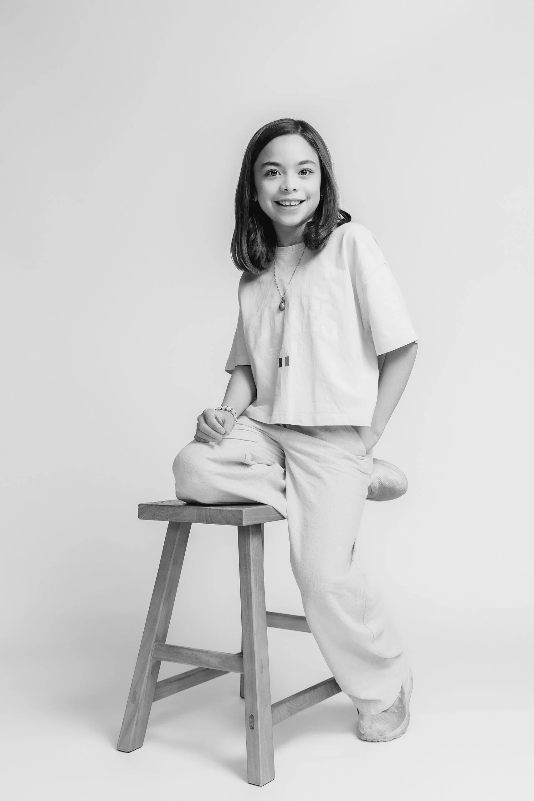 Retrato en blanco y negro de niña sentada en banco, postura relajada y expresión tranquila.