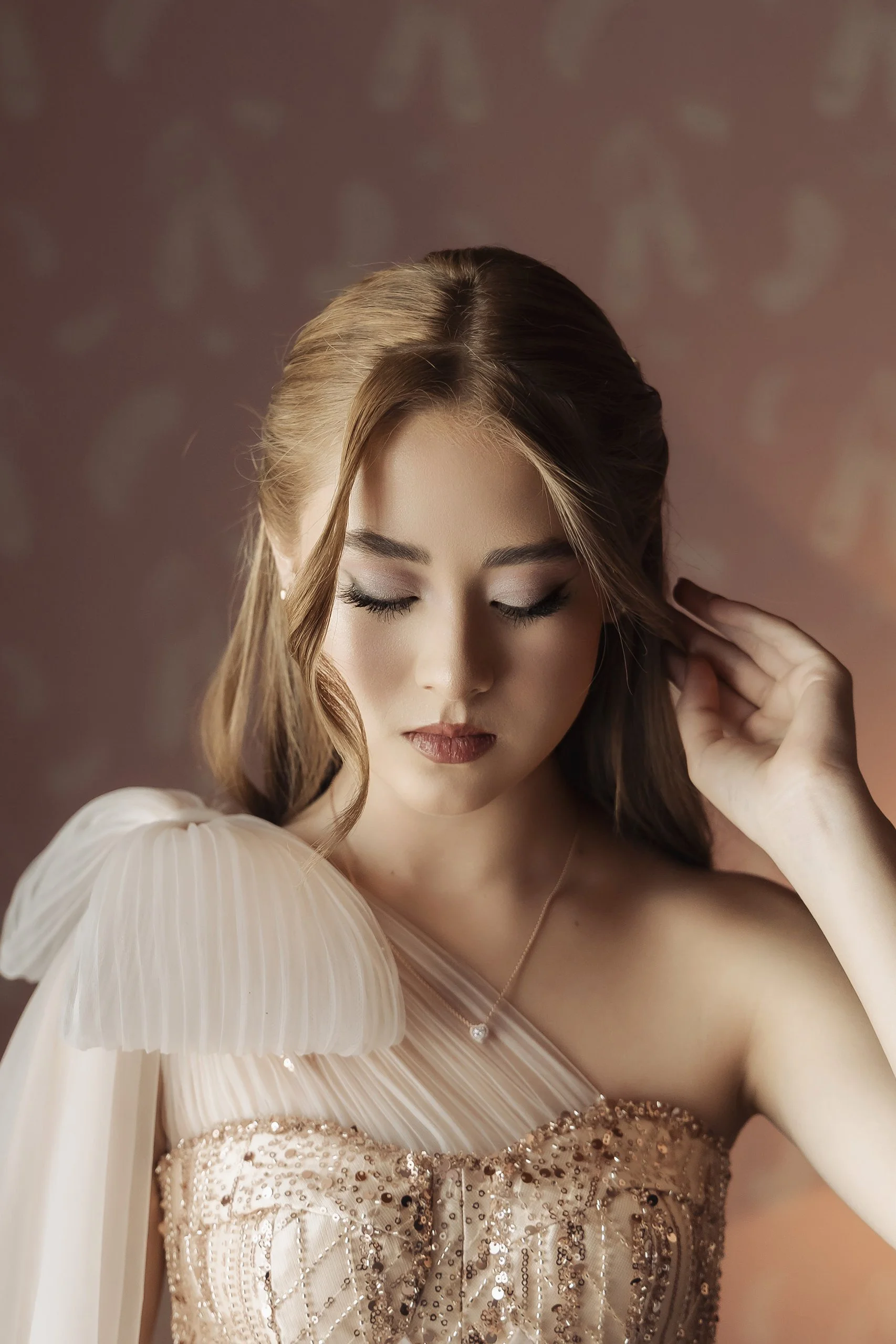 Retrato de mujer en estudio con vestido claro, mirada hacia abajo y gesto delicado.