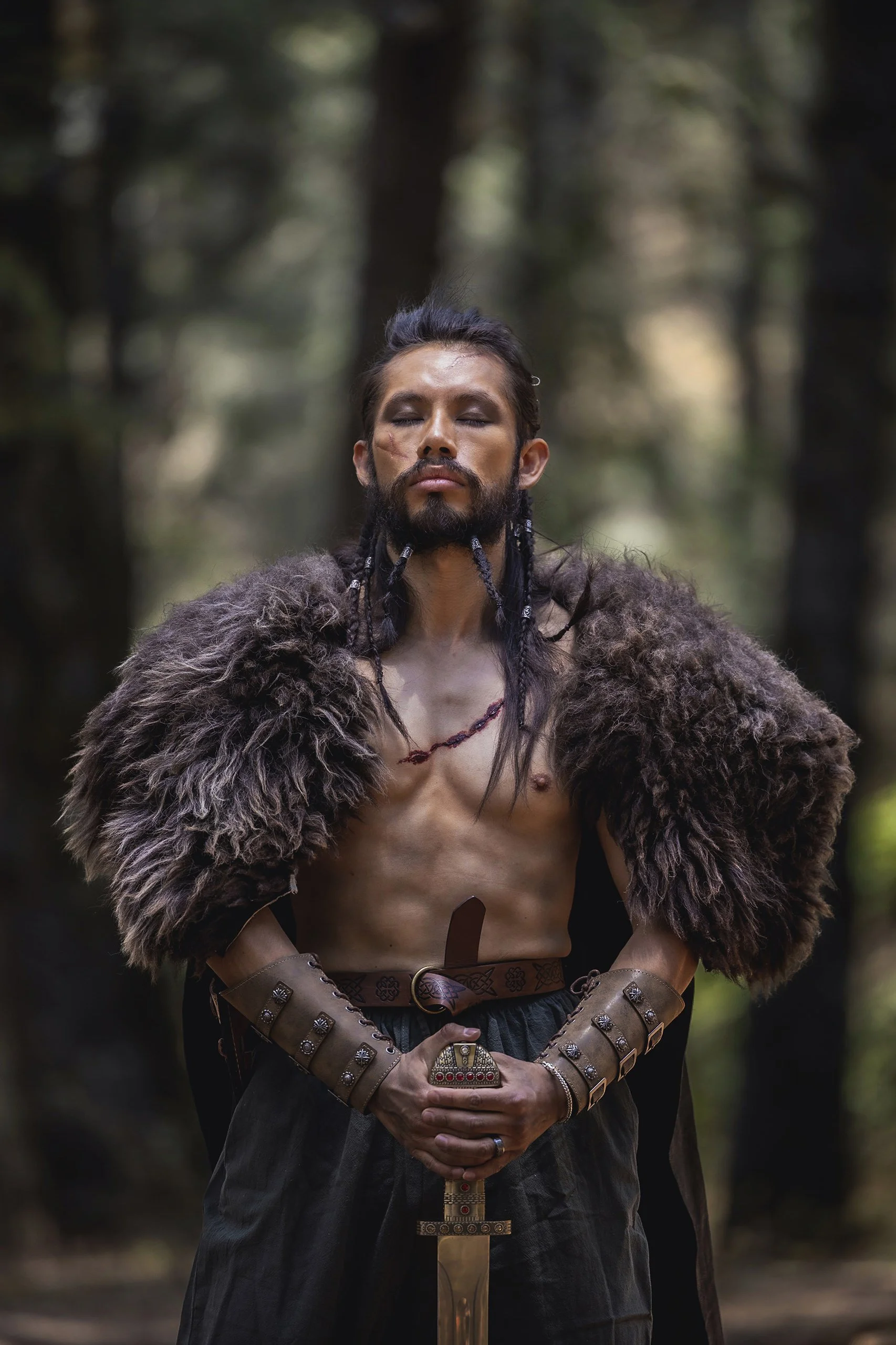 Retrato de hombre en exterior boscoso, torso descubierto, vestimenta ritual y postura frontal.