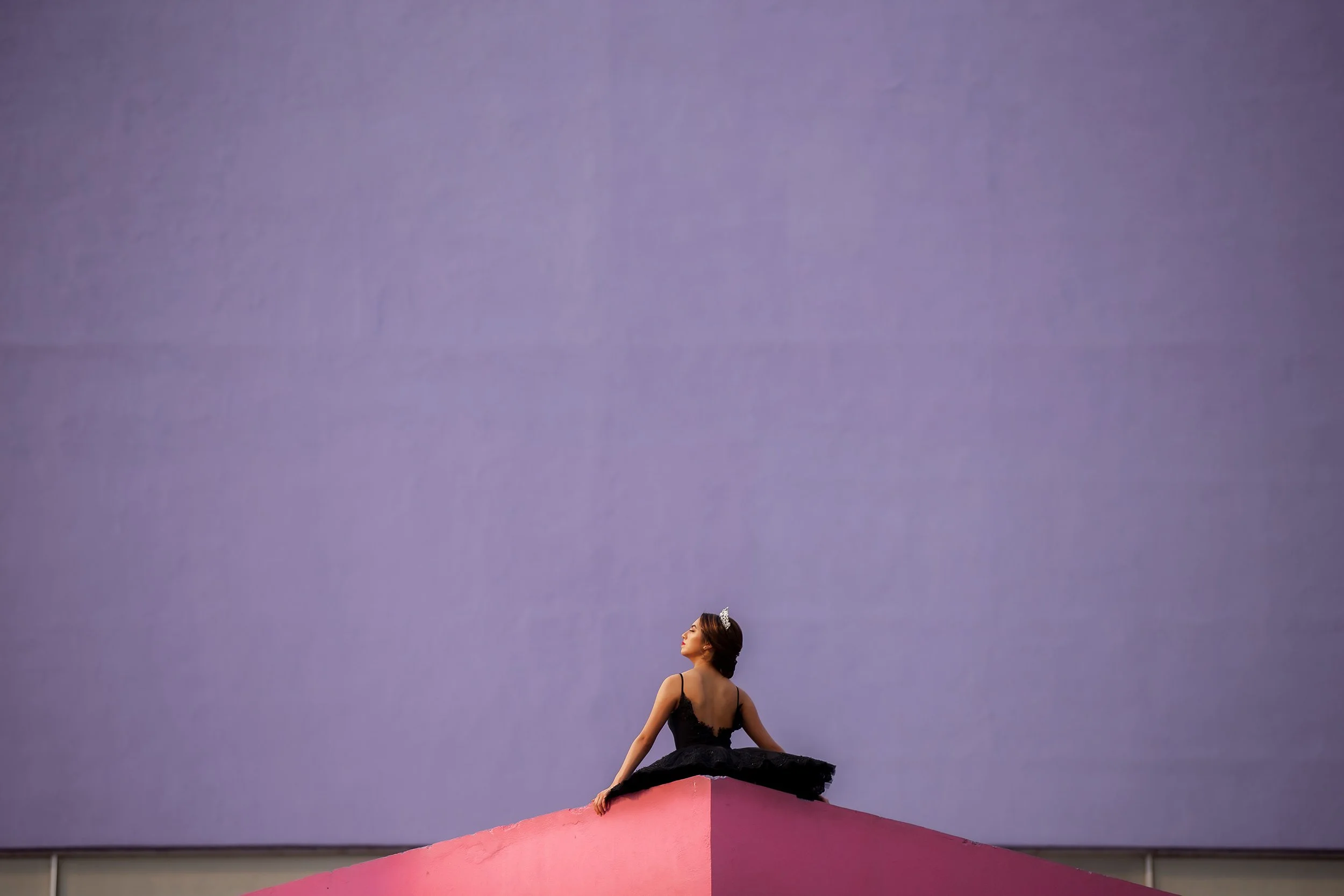 Retrato de mujer sentada en exterior minimalista, figura pequeña frente a fondo liso de color.