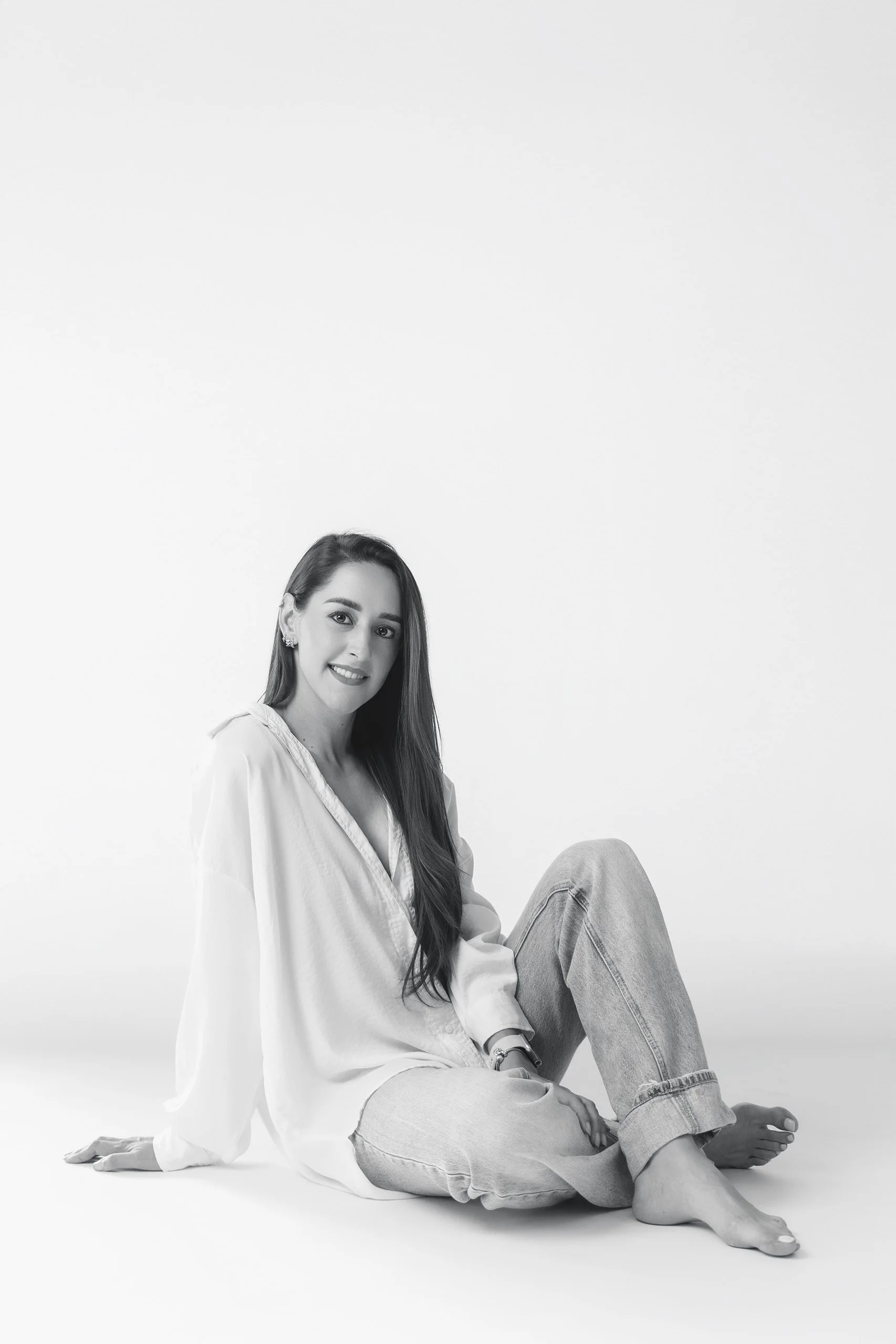 Retrato en blanco y negro de mujer sentada, vestimenta clara y expresión serena frente a fondo blanco.