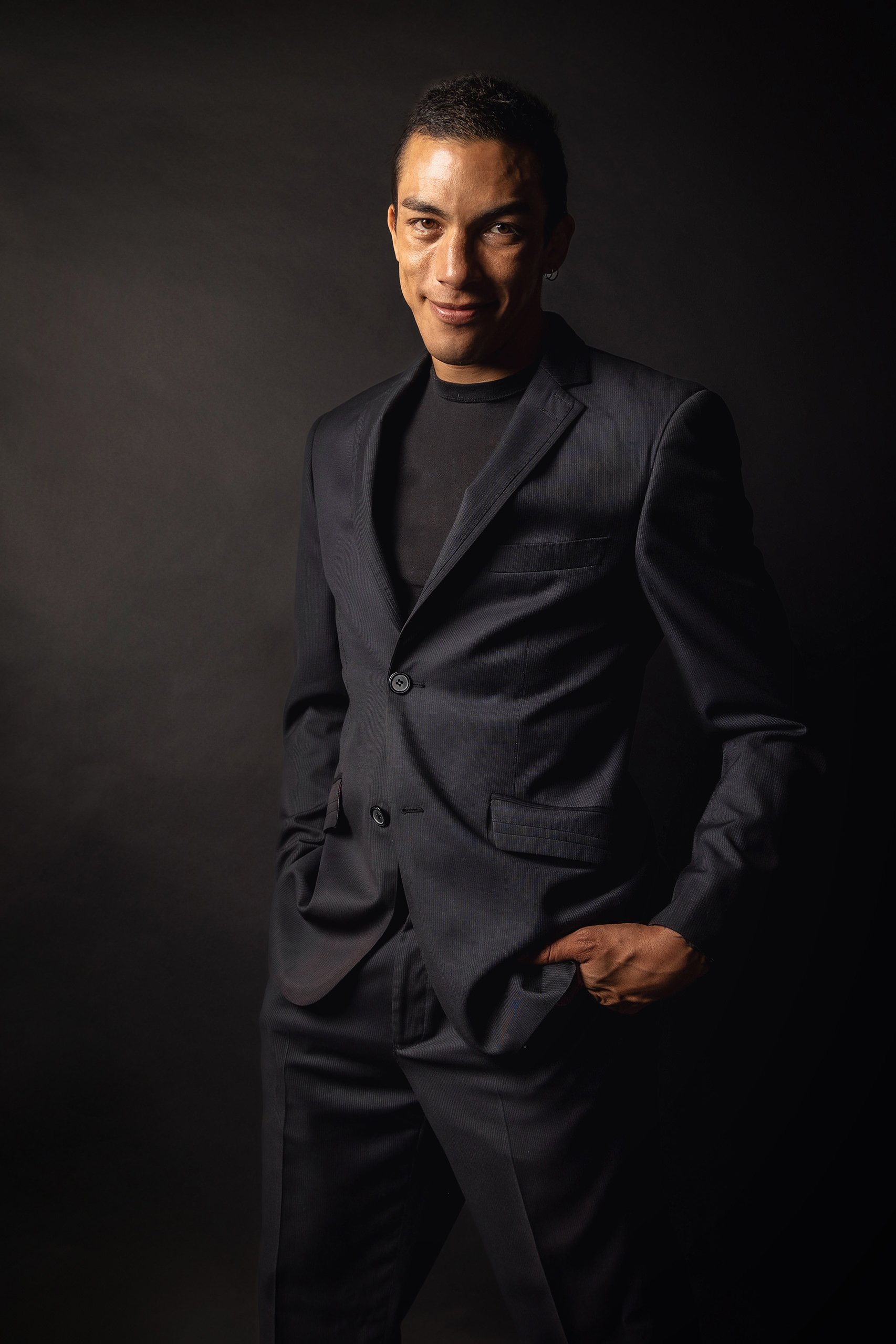 Retrato de hombre en estudio con traje oscuro, encuadre desde el torso y postura relajada.