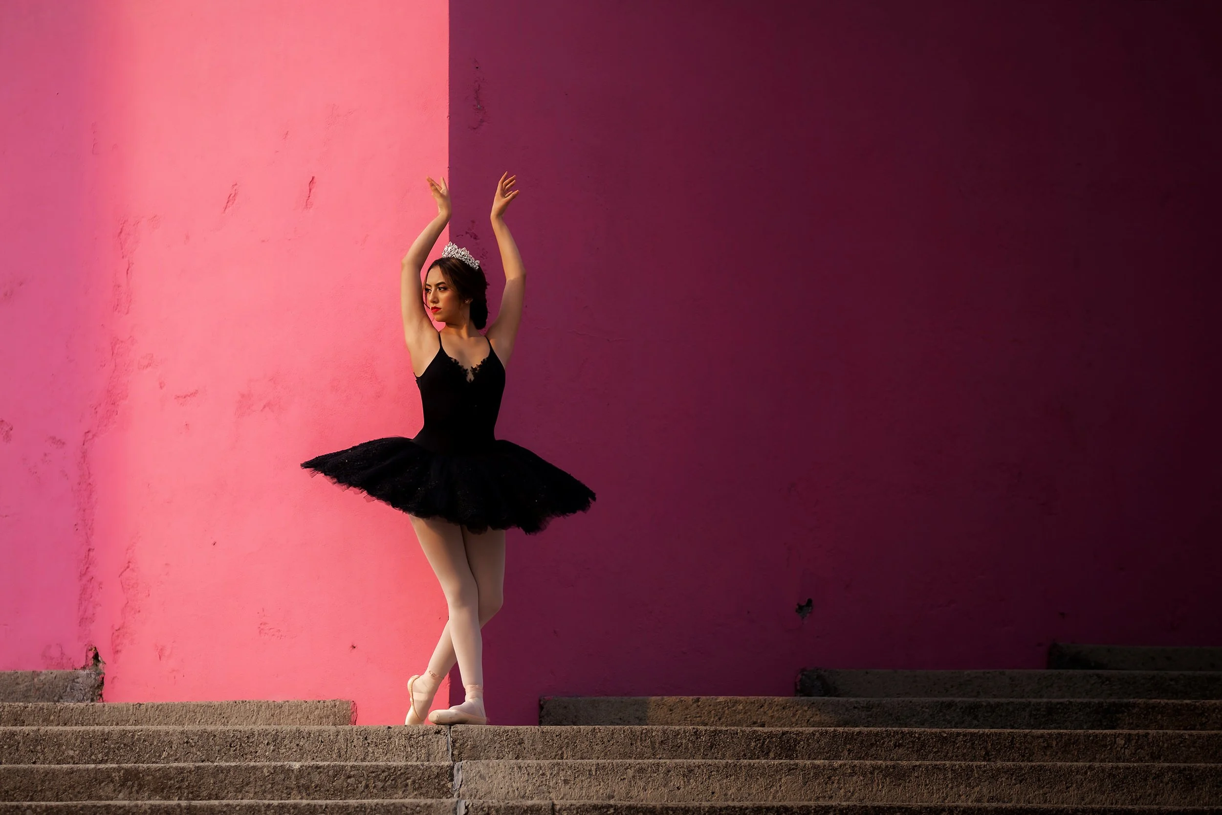 Retrato de mujer bailarina con vestido negro, brazos levantados, fondo geométrico rosa y violeta en exterior.
