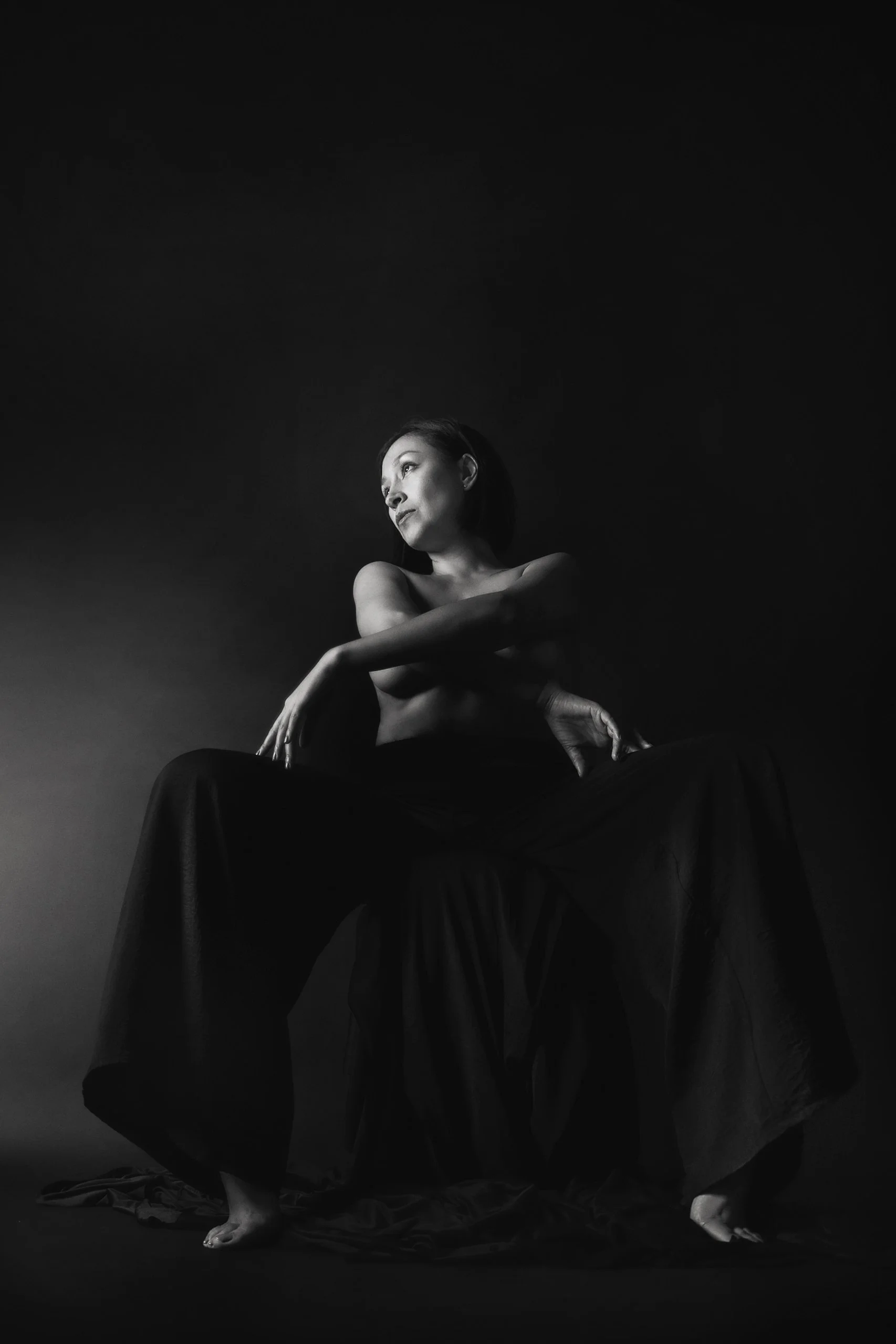 Retrato en blanco y negro de mujer sentada, postura recogida y gesto introspectivo.