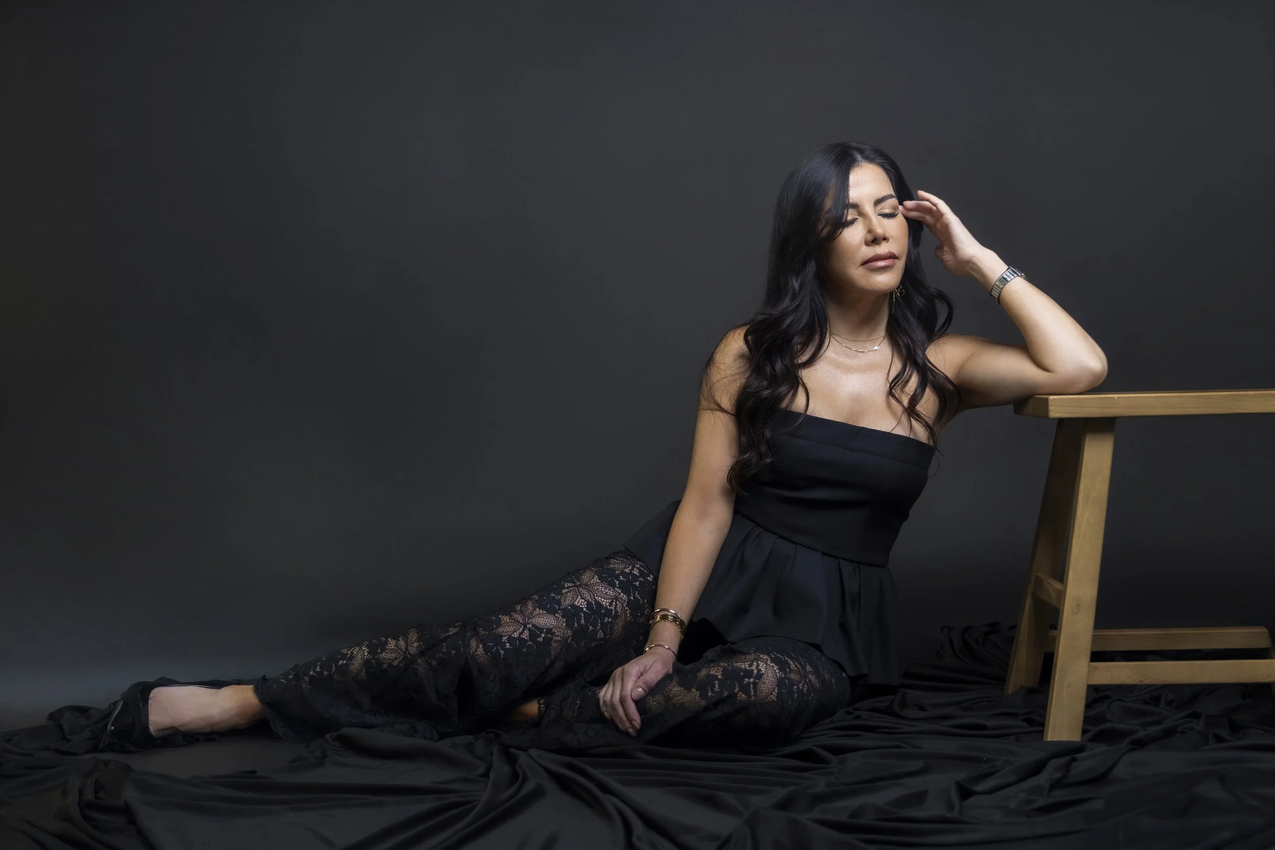 Retrato de mujer recostada en estudio, vestimenta oscura y expresión relajada.